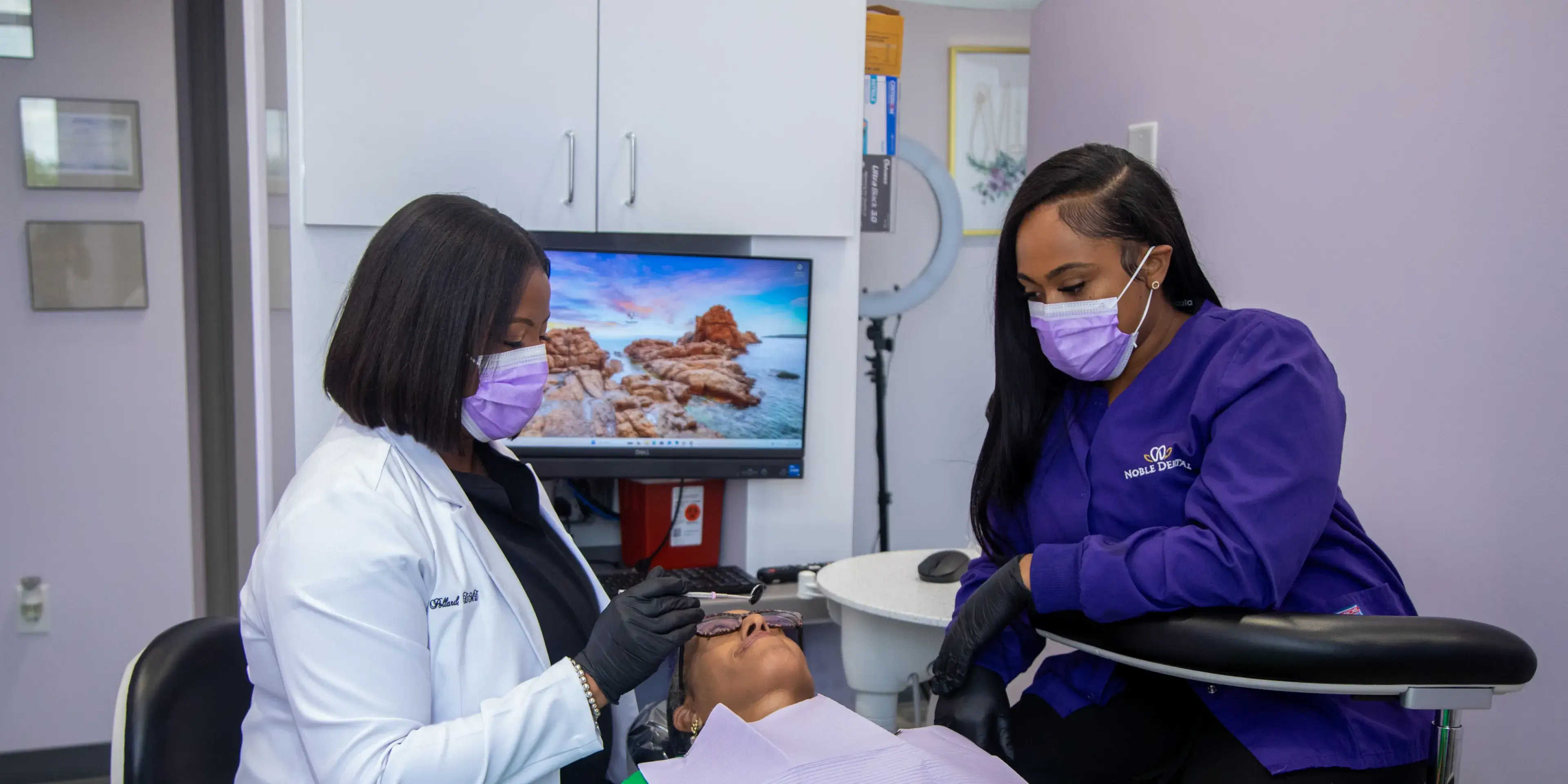 Two dental professionals in masks work on a patient lying in a dental chair.