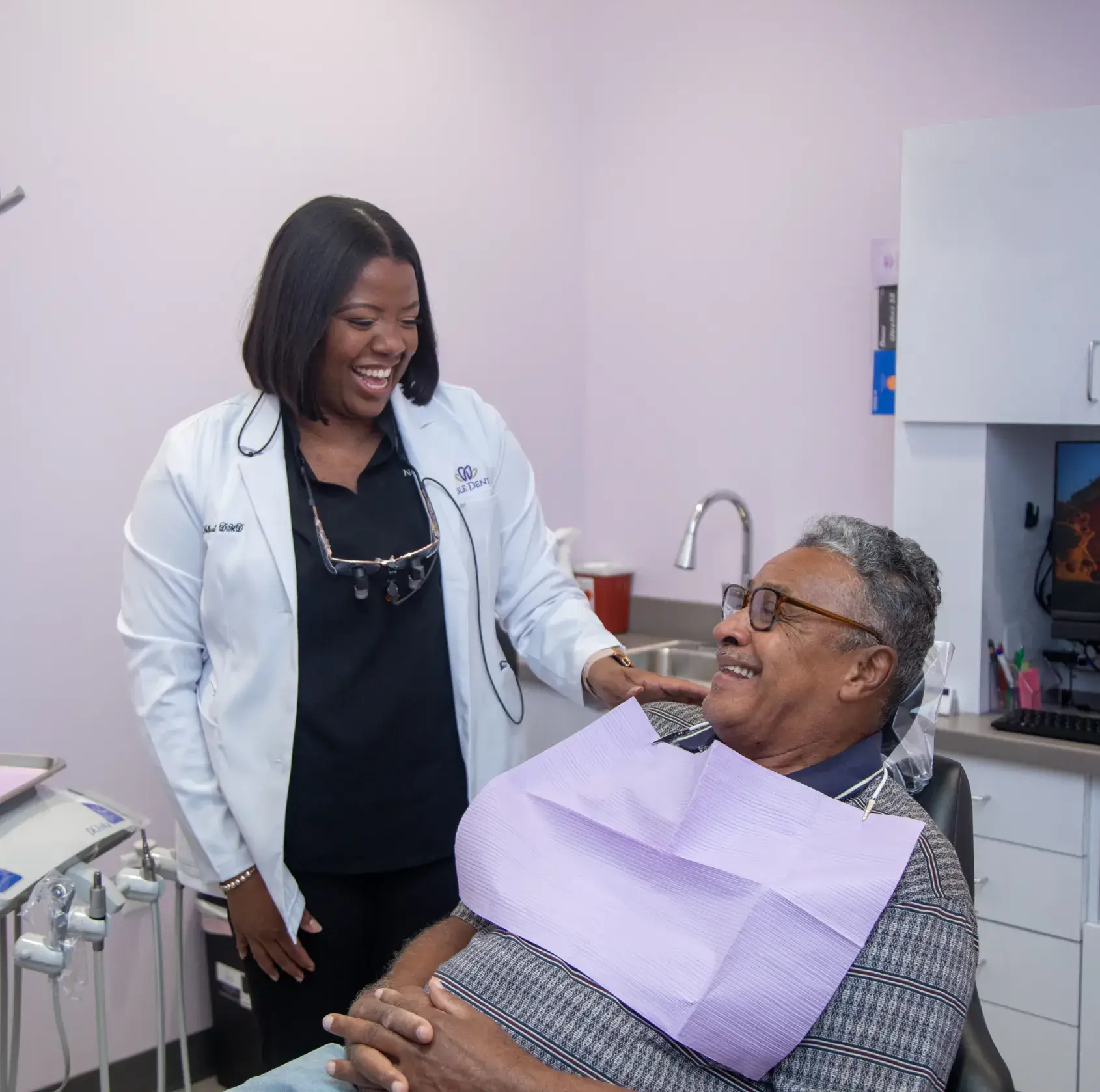 A dentist smiles while talking to a patient seated in a dental chair.