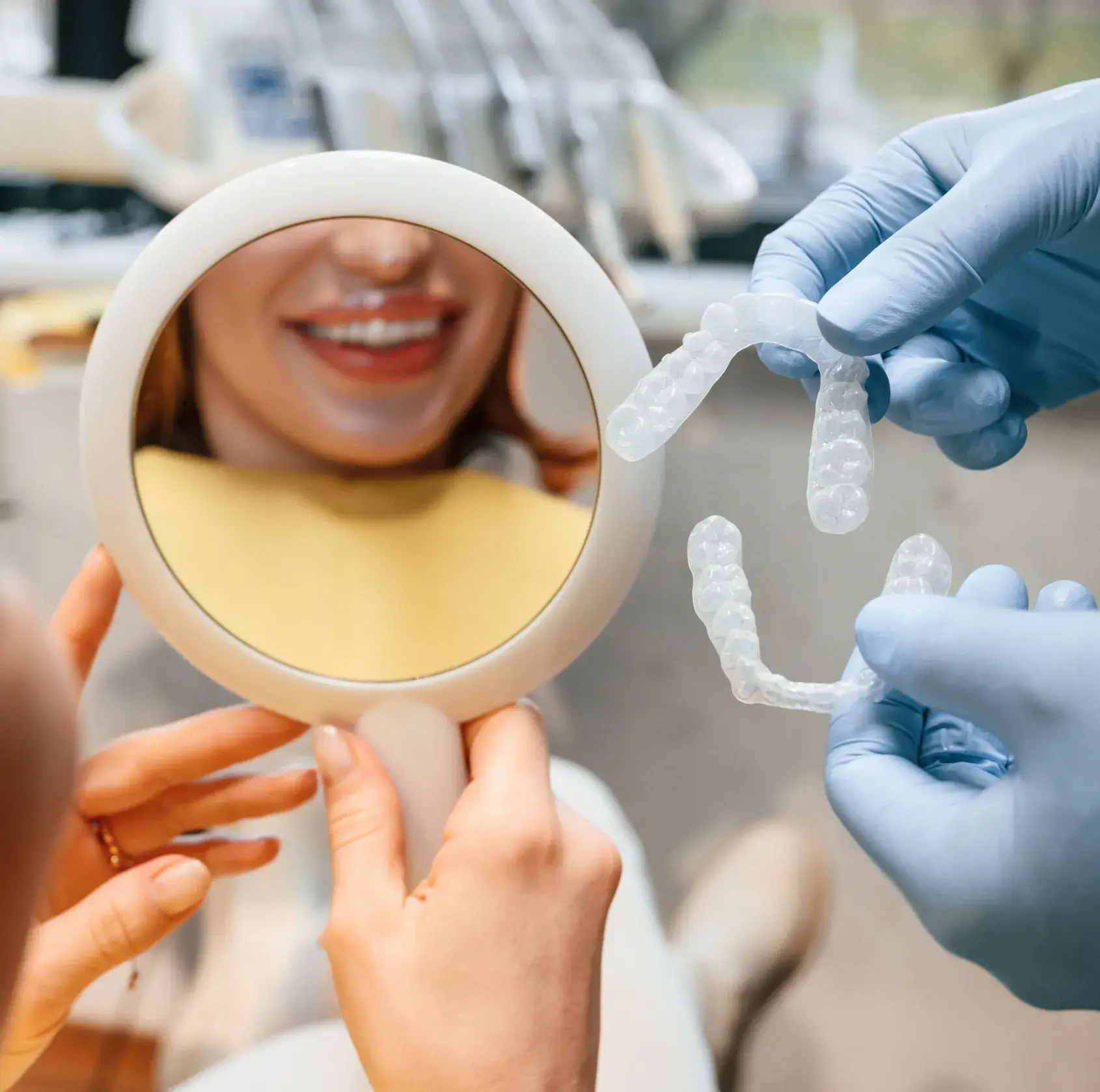 A person holds a mirror and smiles while a dentist shows clear aligners.