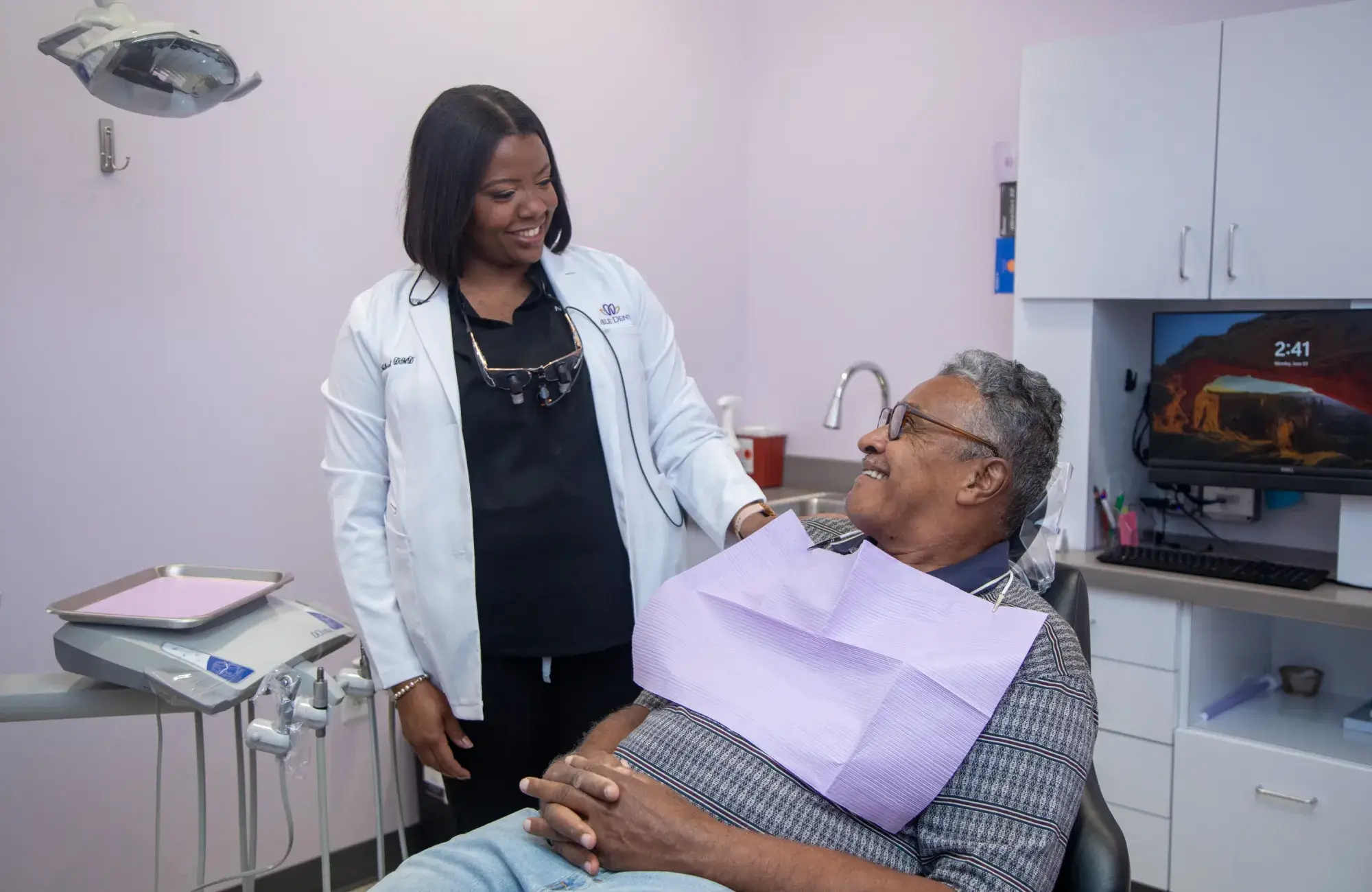 A dentist smiles while talking to a seated patient in a dental office.