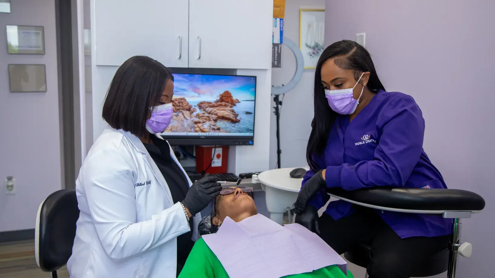 Two dental professionals wearing masks work on a patient lying in a dental chair.