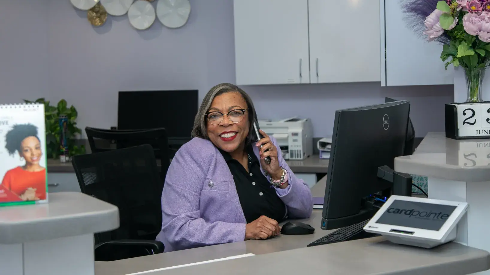 A woman at a reception desk is smiling and talking on the phone.