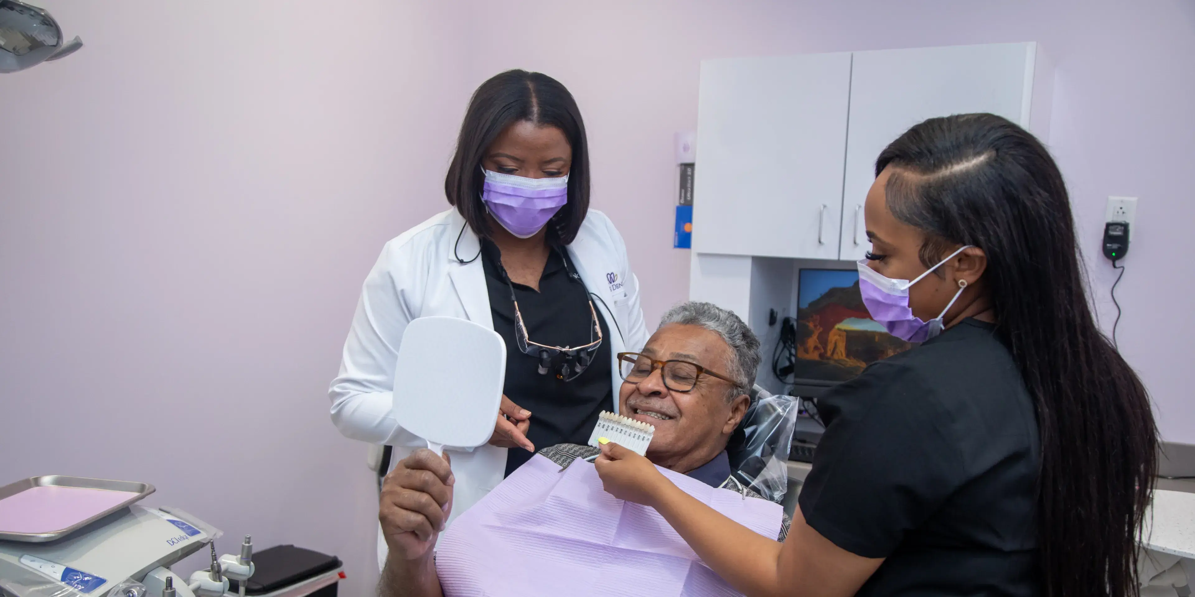 A dentist and assistant help a patient match teeth color using a shade guide.