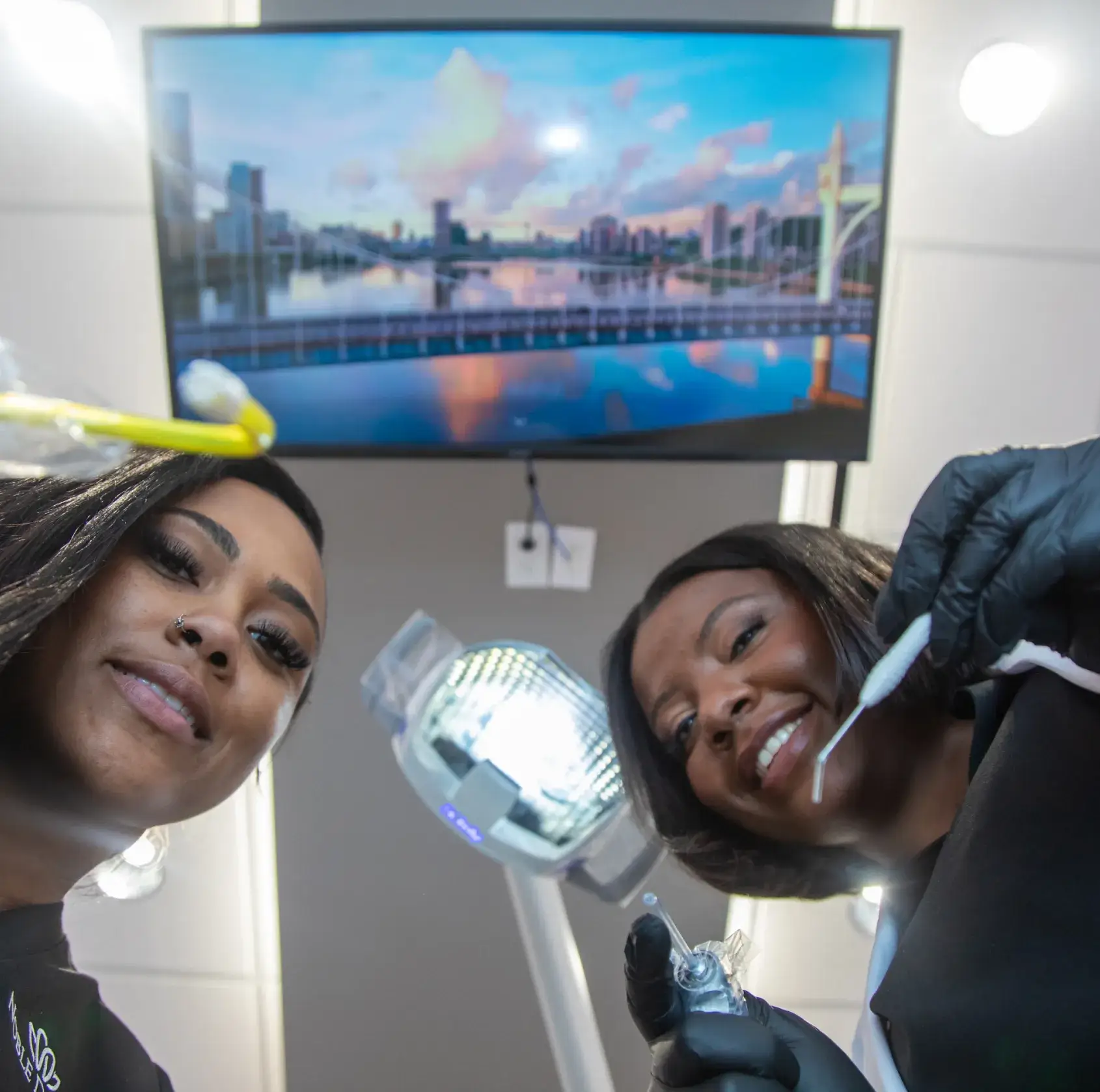 Two dental professionals, wearing gloves, smile as they prepare dental tools in a clinic.