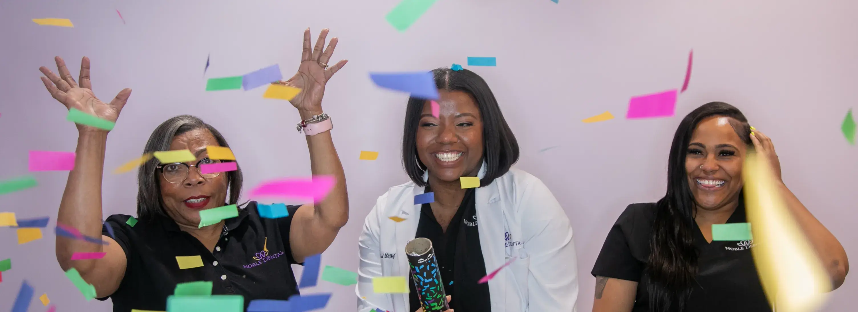 Three women smiling and celebrating as colorful confetti falls around them.