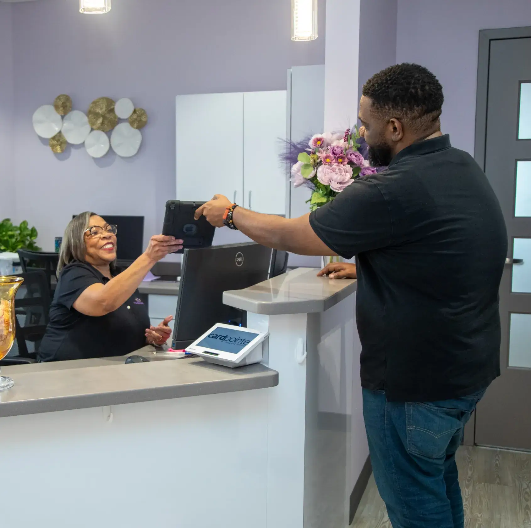 A man hands his phone to a receptionist at a front desk in an office setting.