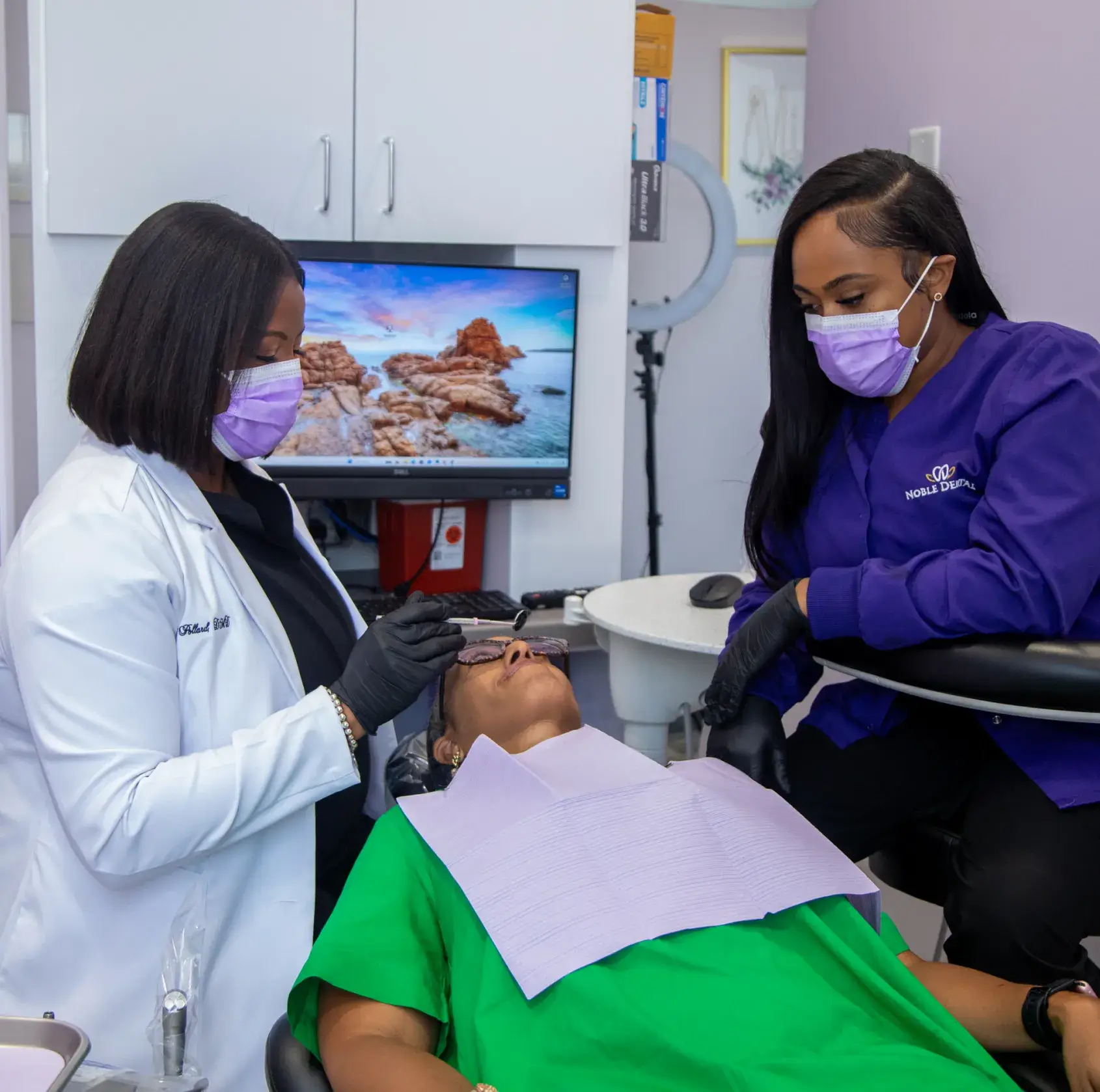 Two dental professionals in masks examine a patient's teeth in a dental office.