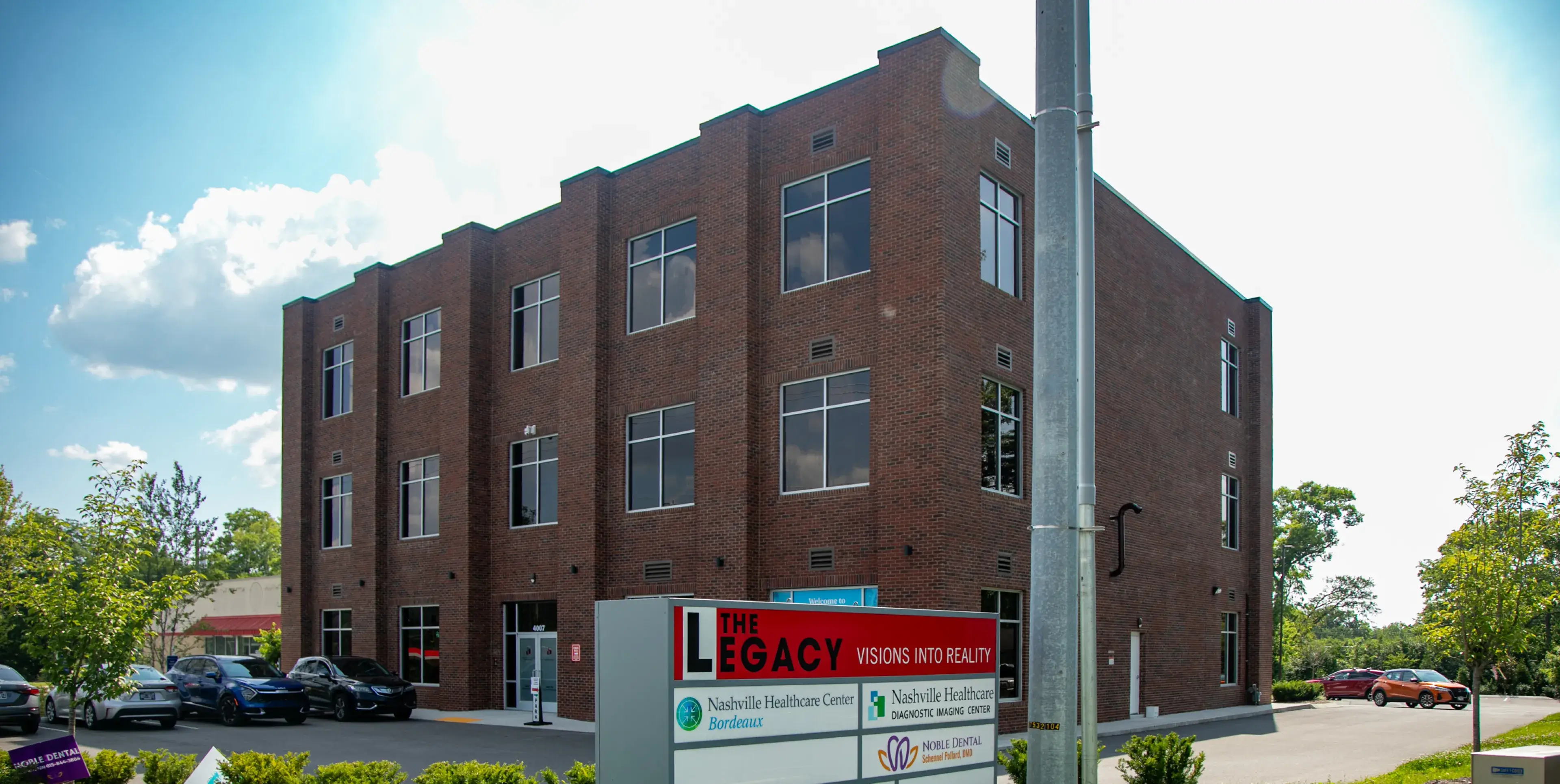 A three-story brick building with a sign in front reads "The Legacy."