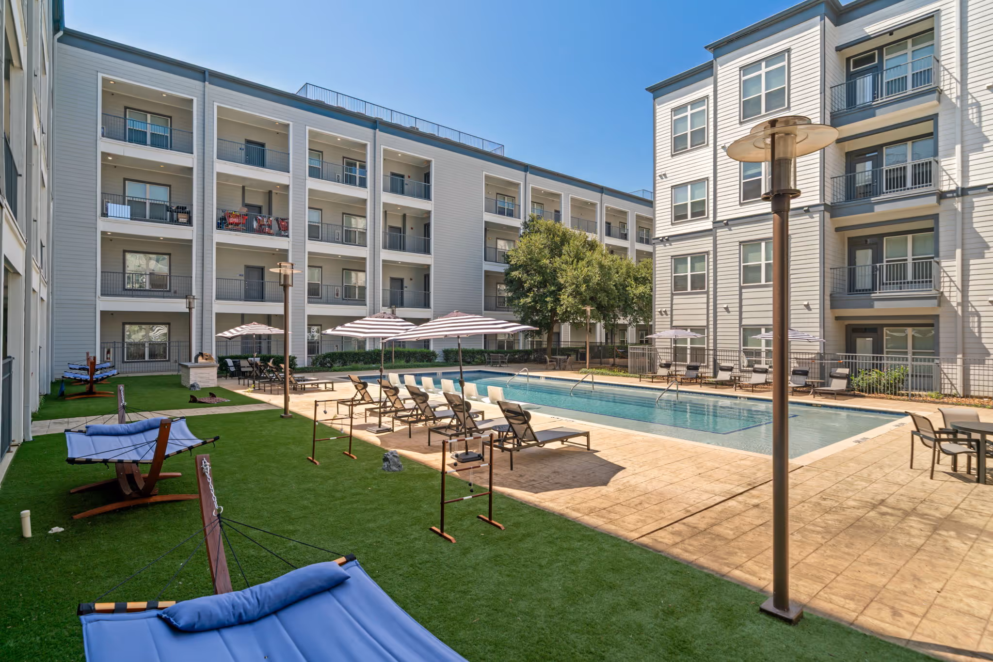Courtyard amenity space featuring a swimming pool, lounge chairs, umbrellas, and a turf area with hammocks.
