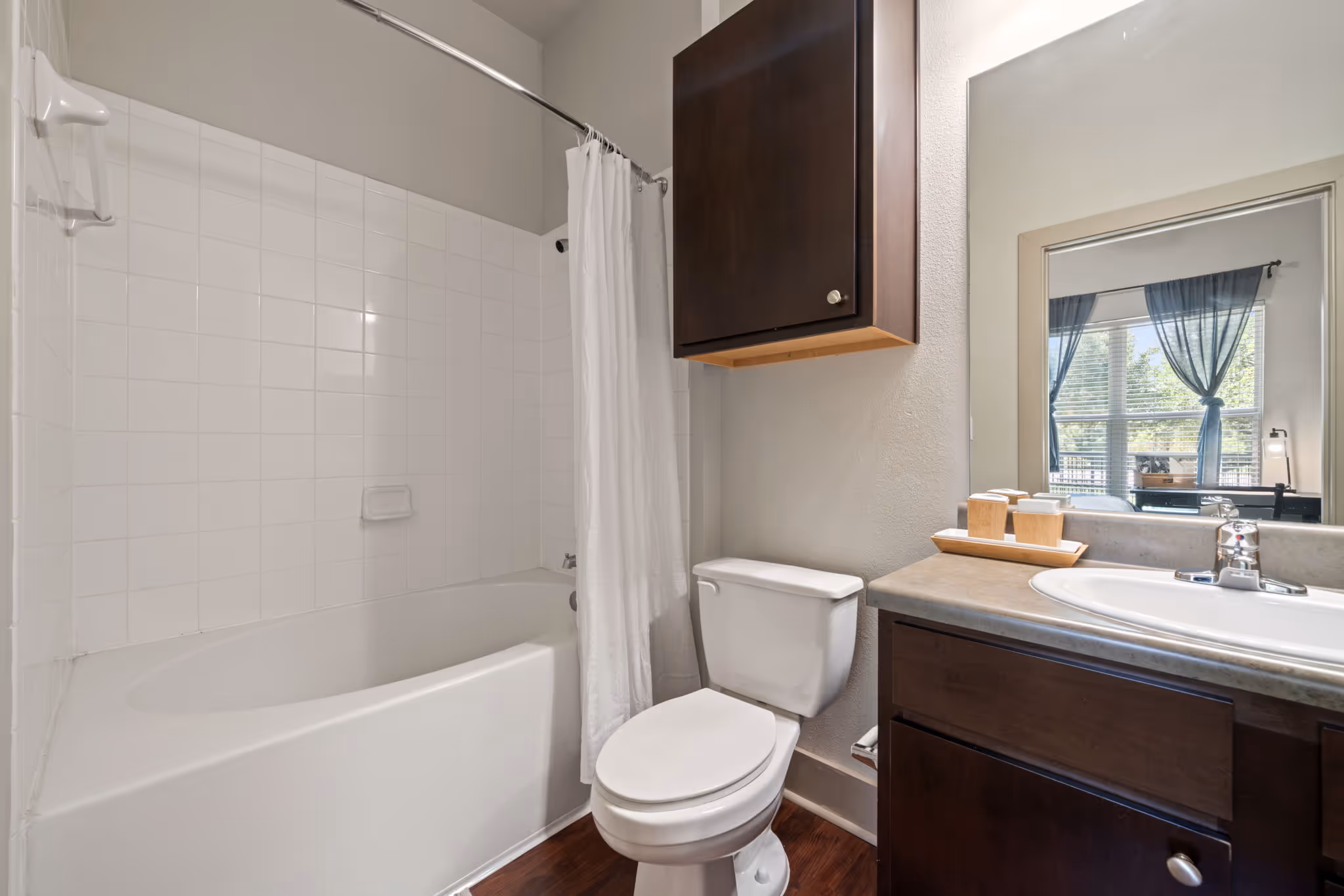 Clean apartment bathroom with large mirror and integrated storage cabinets at The Lofts at Wolf Pen Creek.