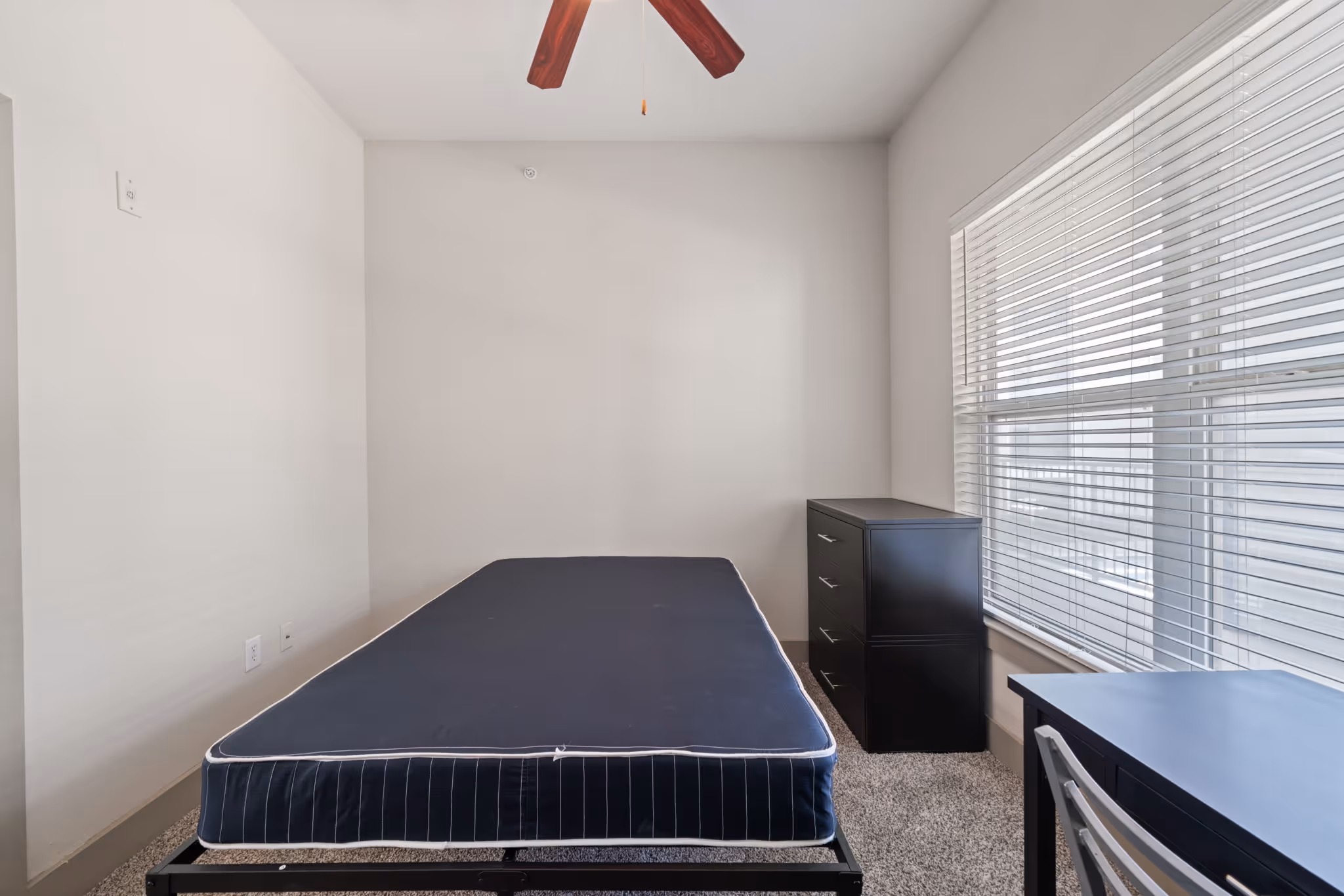 Minimalist bedroom setup with a large window and a dark wood dresser at The Lofts at Wolf Pen Creek.