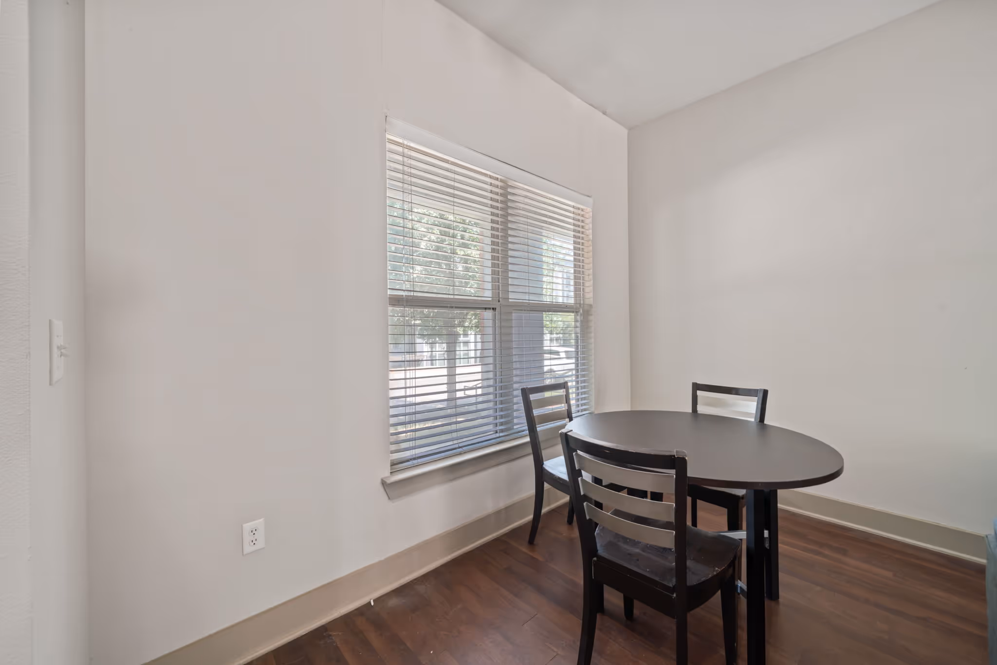 Dining area with a circular table and chairs near a window with blinds at The Lofts at Wolf Pen Creek.