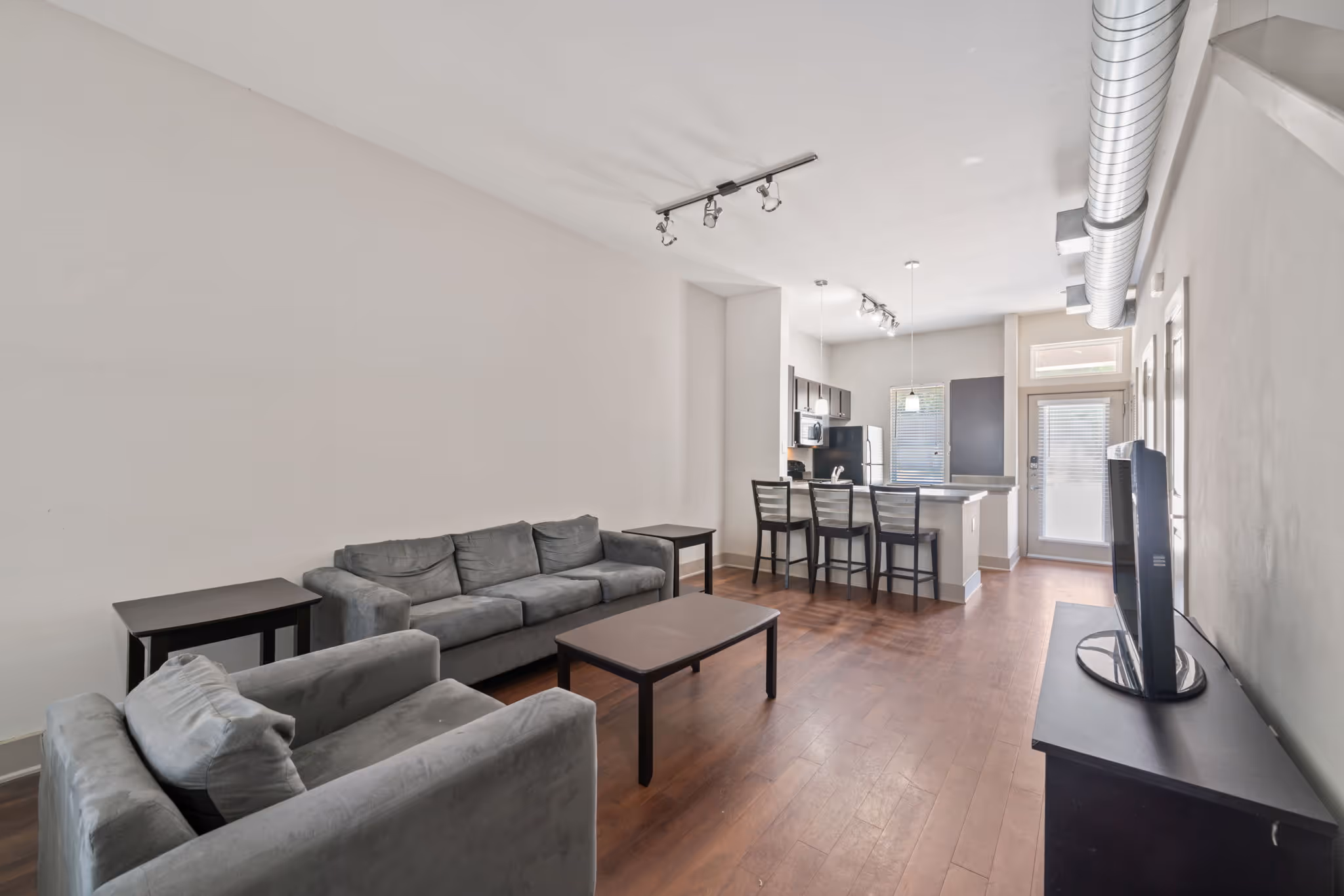 Living room setup featuring a gray sofa and armchair with views of the kitchen bar.