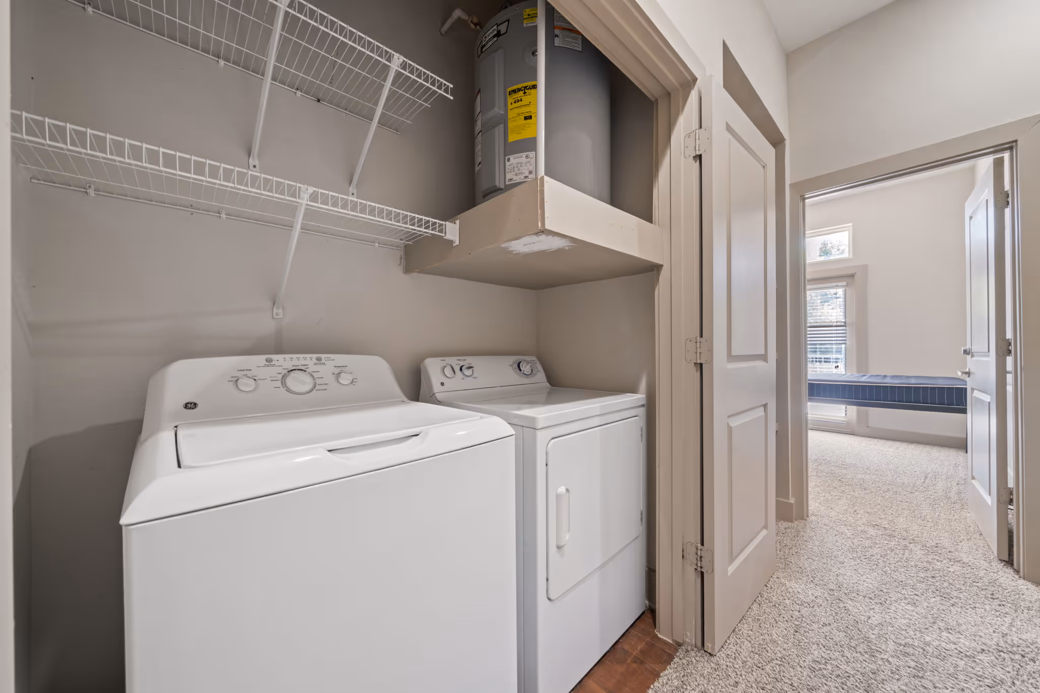 In-unit laundry closet at The Lofts at Wolf Pen Creek featuring full-size washer and dryer units and built-in shelving.