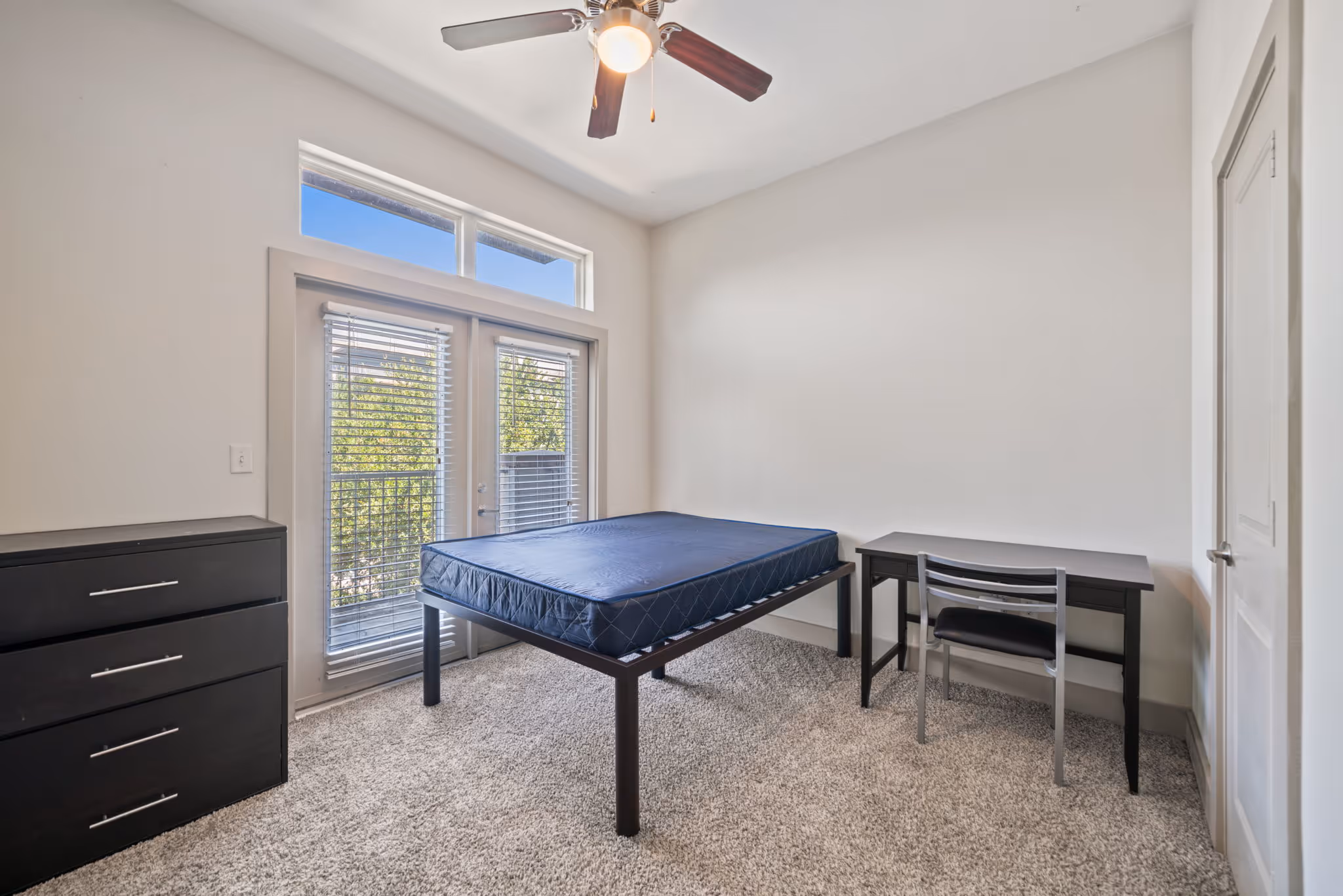 Well-lit bedroom in College Station showing a bed frame, dresser, and private workspace.