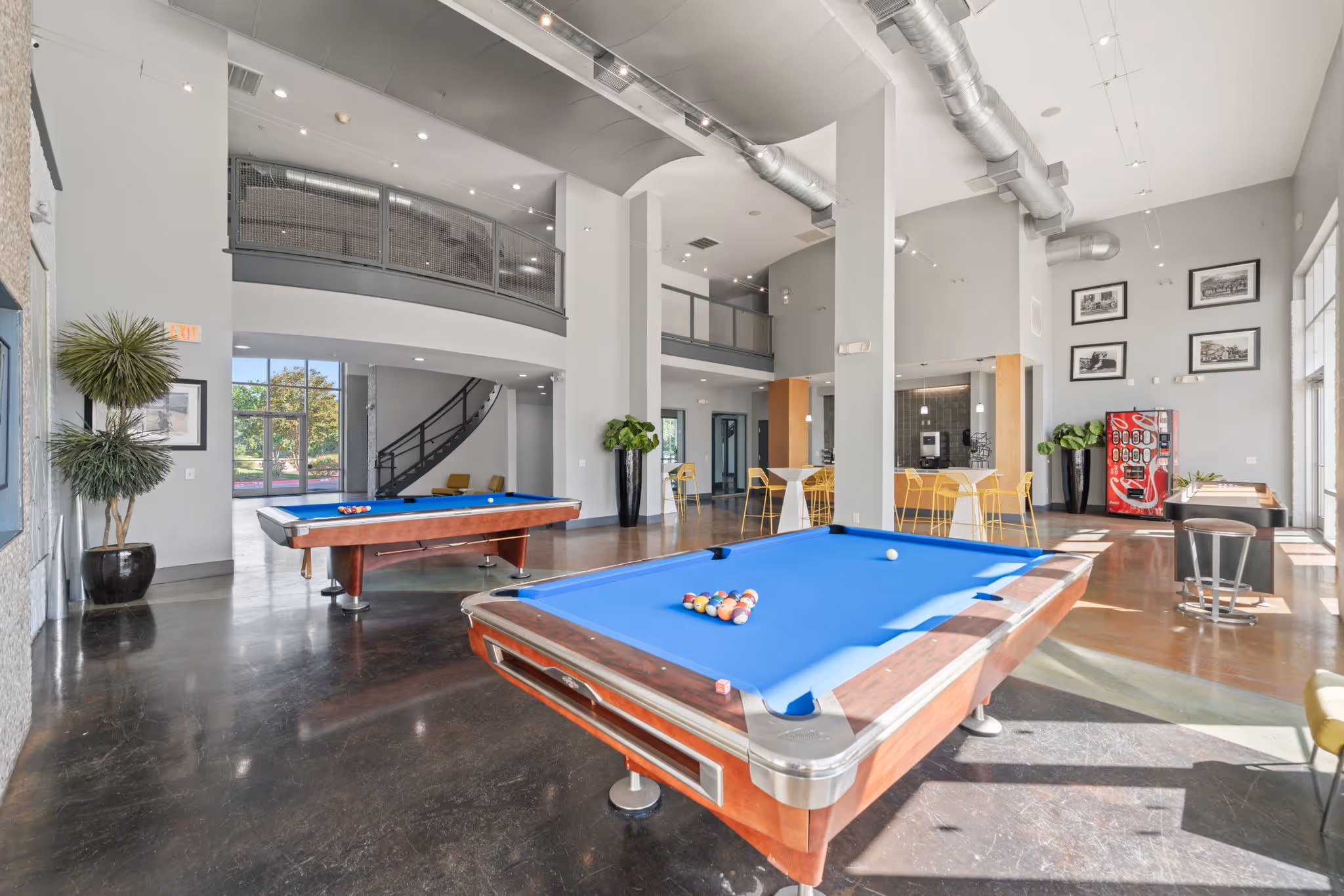 Expansive game room at The Lofts at Wolf Pen Creek in College Station, featuring blue-felt pool tables, and a refreshment area.