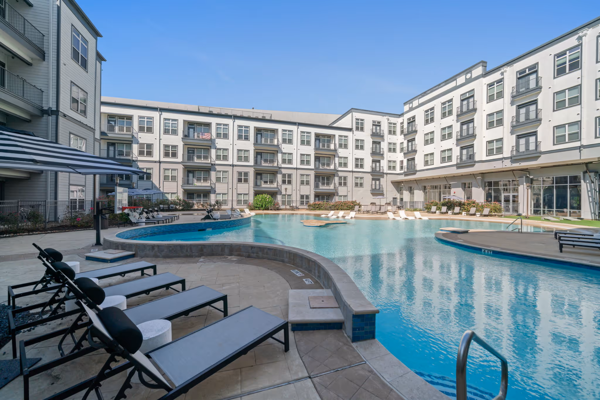 Relaxing poolside setting at The Lofts at Wolf Pen Creek in College Station, TX, featuring blue-tiled accents and striped umbrellas.