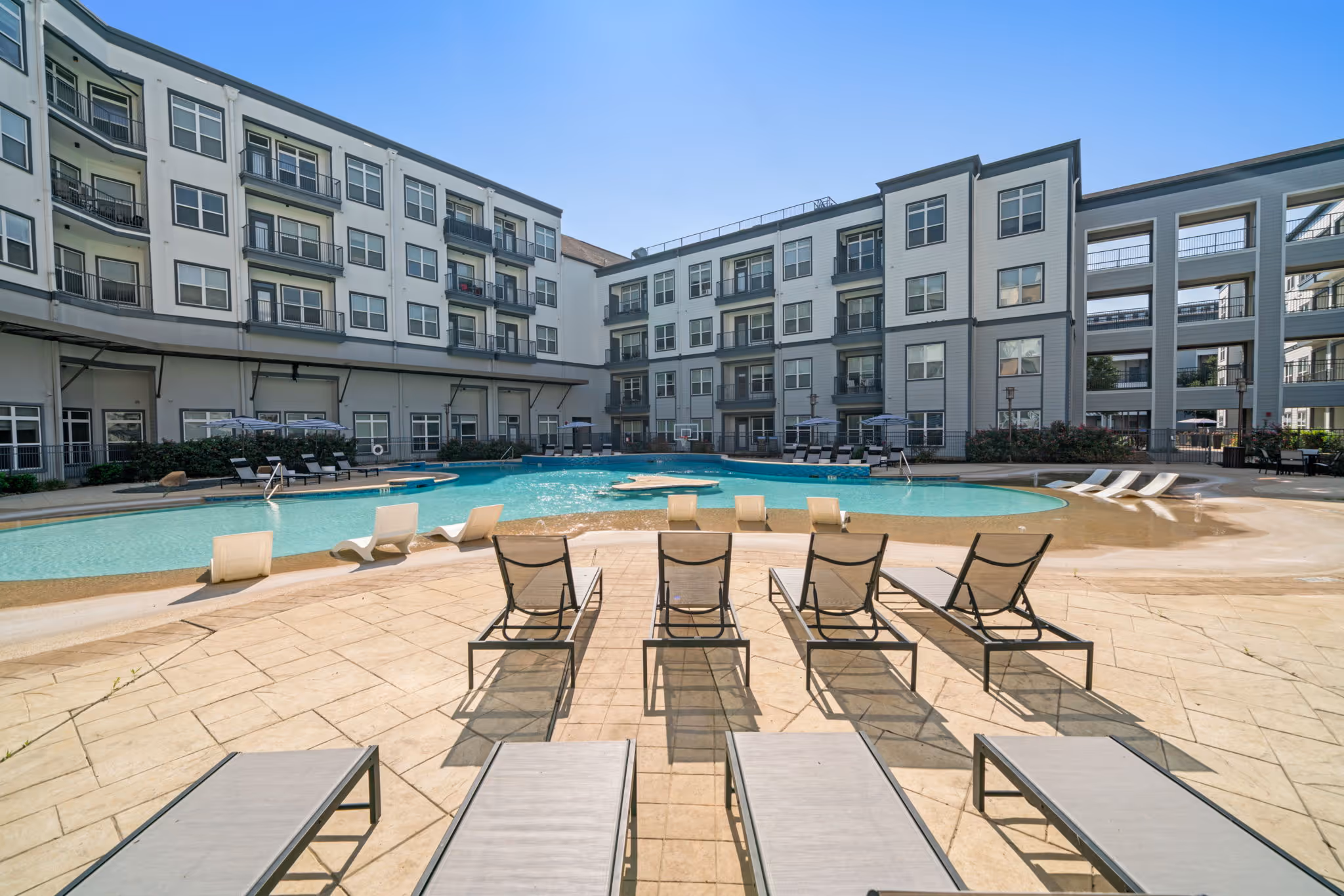 Sunny courtyard and expansive pool deck at The Lofts at Wolf Pen Creek, offering multiple lounge areas for residents in College Station.