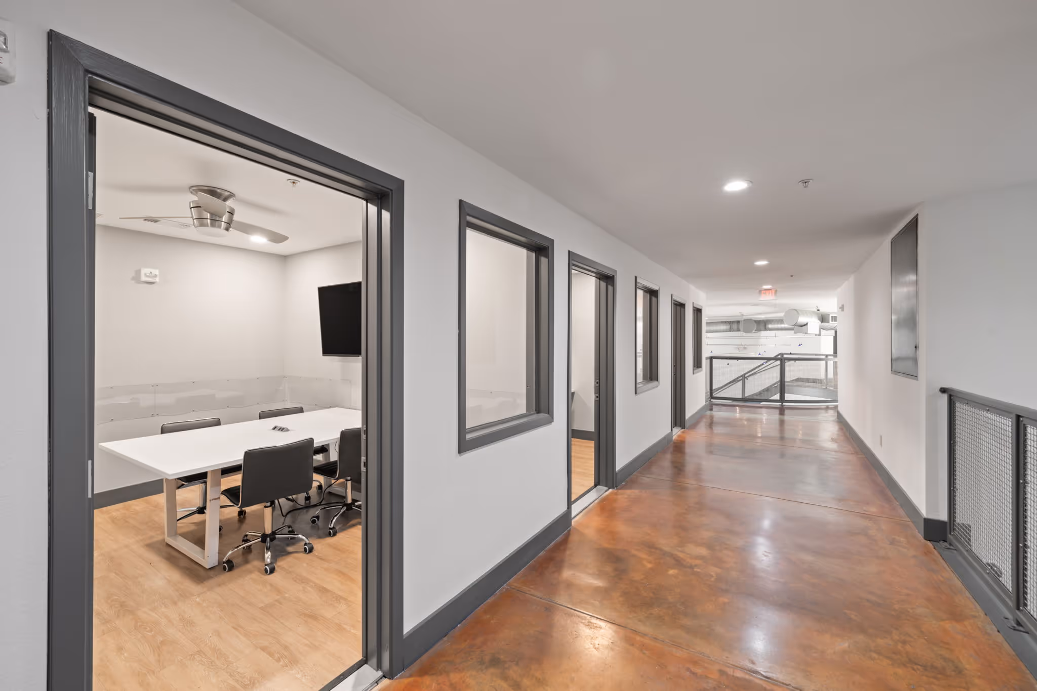 Interior hallway at The Lofts at Wolf Pen Creek apartments leading to private glass-walled study rooms and conference spaces.