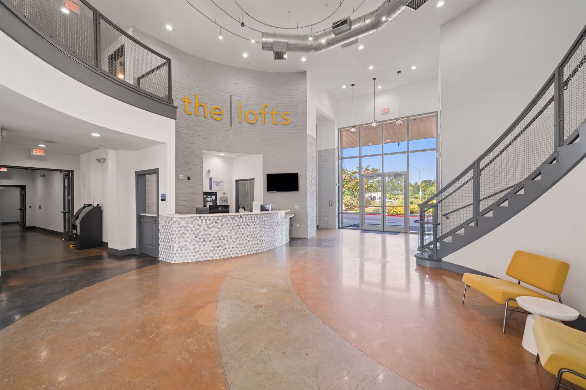 Bright, high-ceilinged entrance lobby at The Lofts at Wolf Pen Creek in College Station, TX, with "the lofts" signage on a gray brick accent wall.