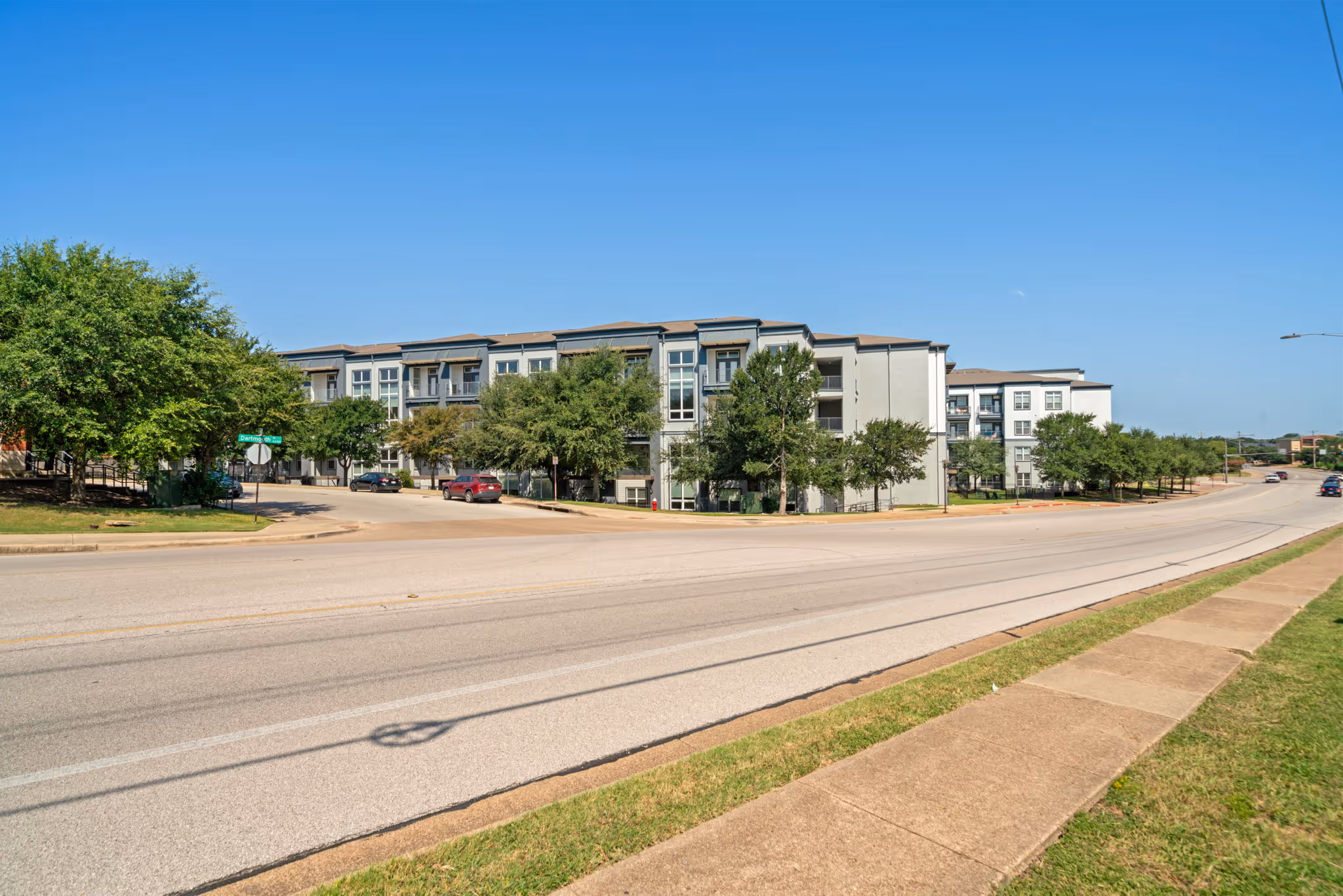 Long-range view of the multi-level apartment buildings at The Lofts at Wolf Pen Creek along a tree-lined road in College Station.