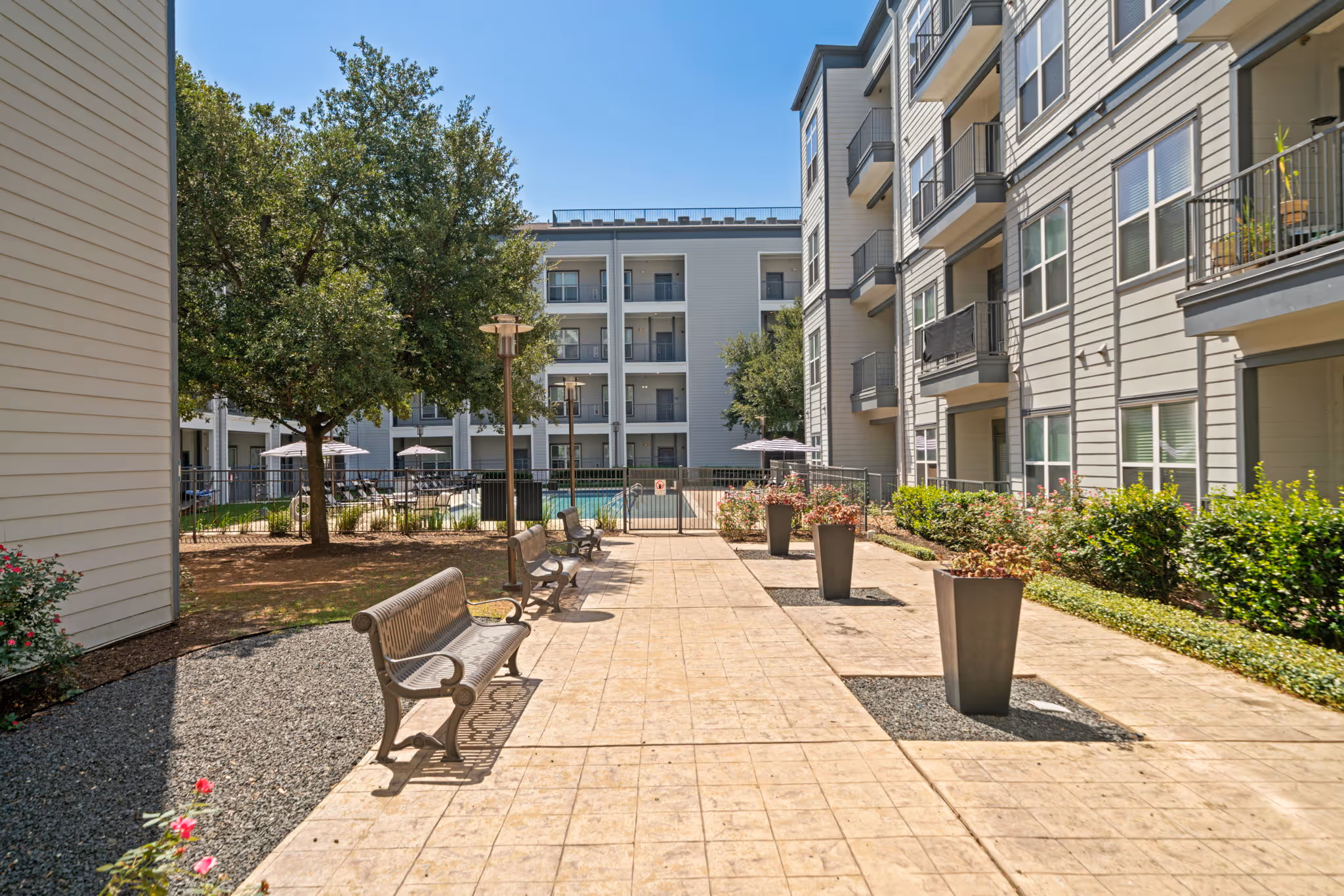 Outdoor walking path and courtyard with benches and potted plants at The Lofts at Wolf Pen Creek apartments.