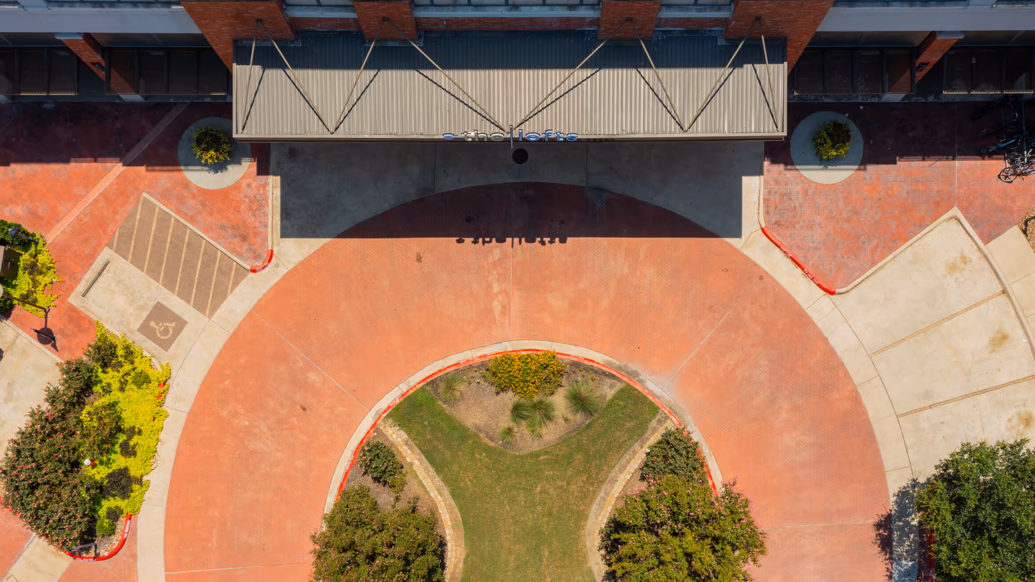 Top-down aerial view of the main leasing office entrance at The Lofts at Wolf Pen Creek, featuring a circular driveway and designated guest parking in College Station, TX.