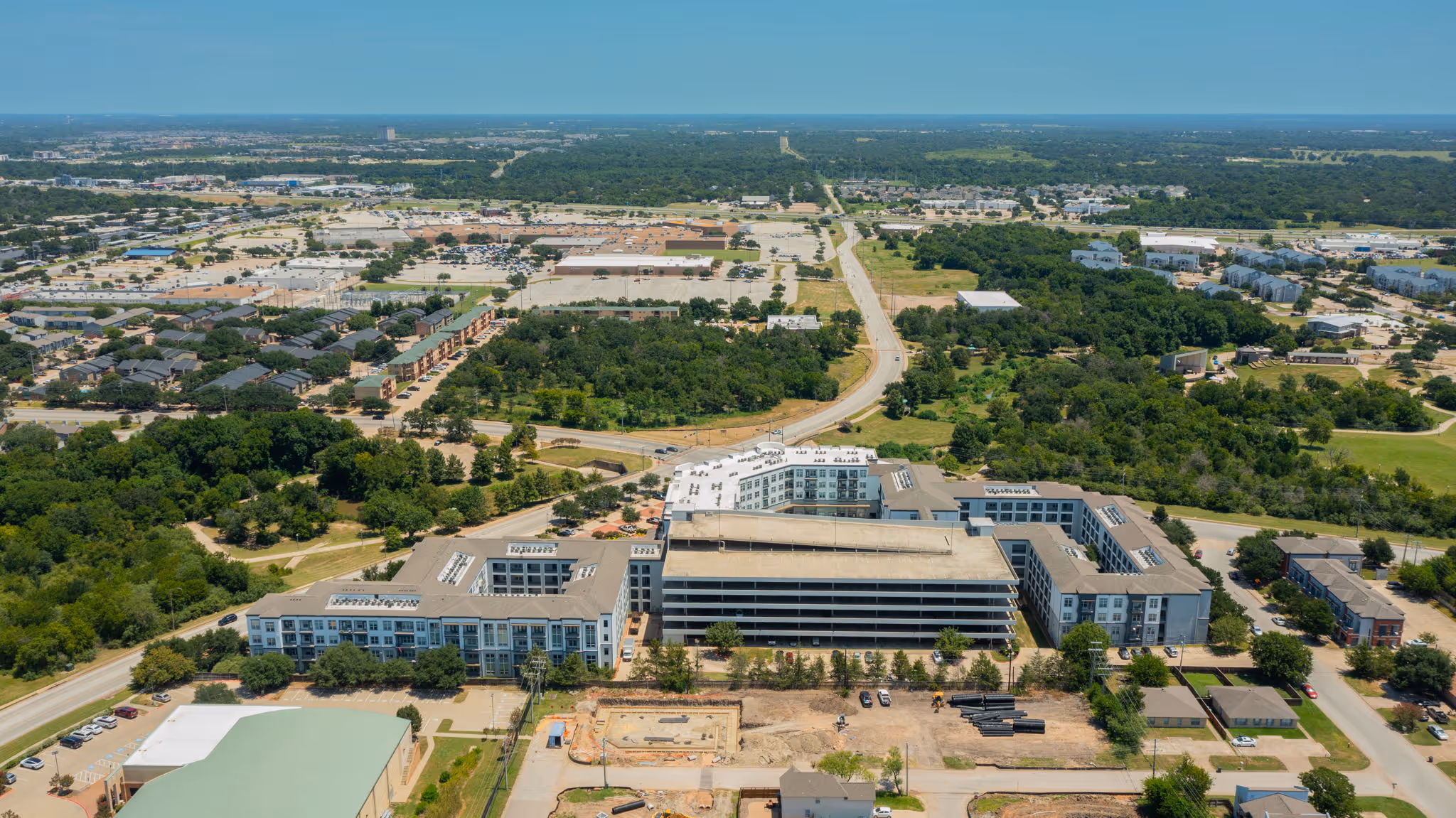 Aerial overview of the multi-wing apartment complex, neighborhood, and parking garage at The Lofts at Wolf Pen Creek. 