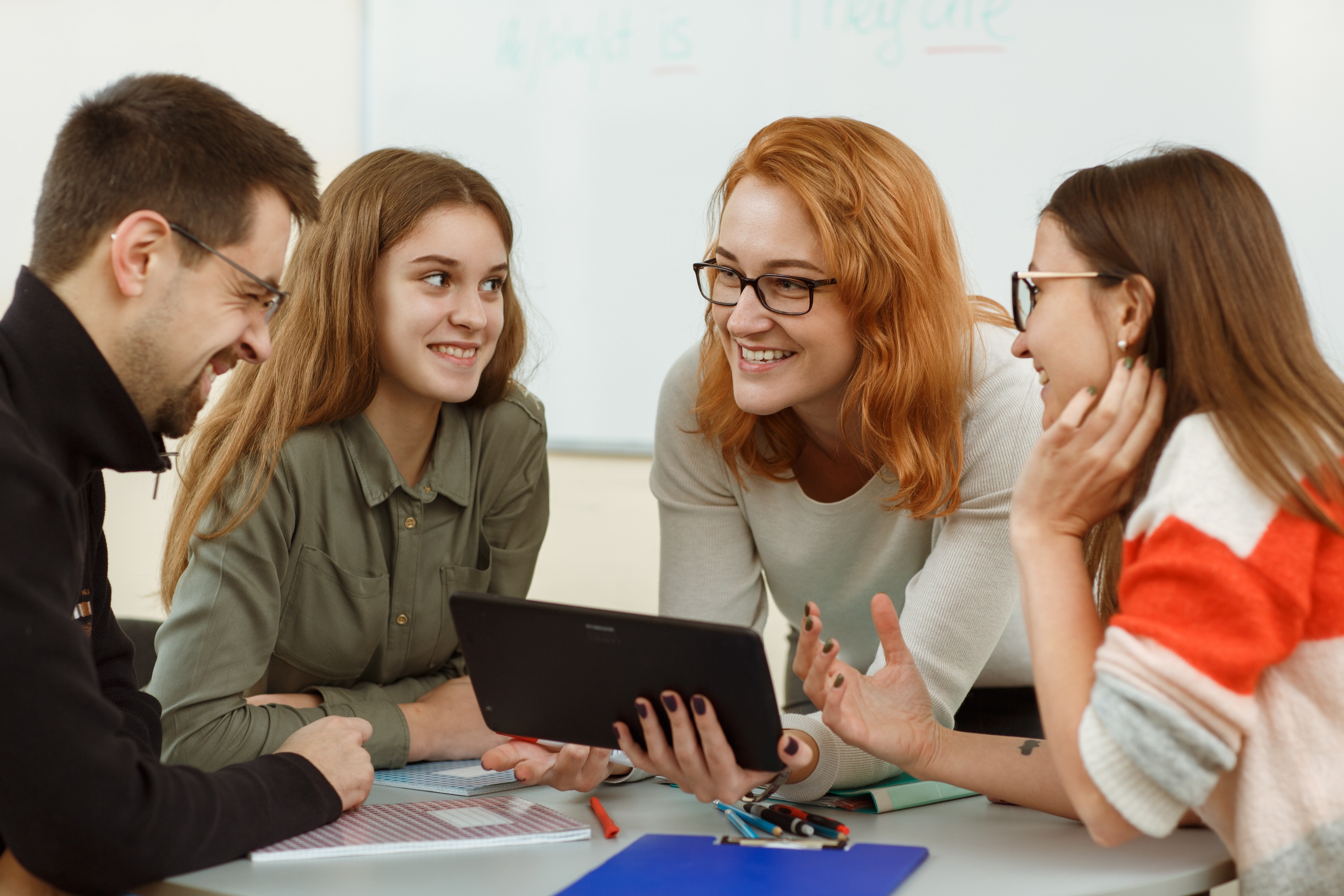 A group of students collaborating with a tablet in a private study room at The Lofts at Wolf Pen Creek, featuring the community’s modern academic spaces near Texas A&M University.