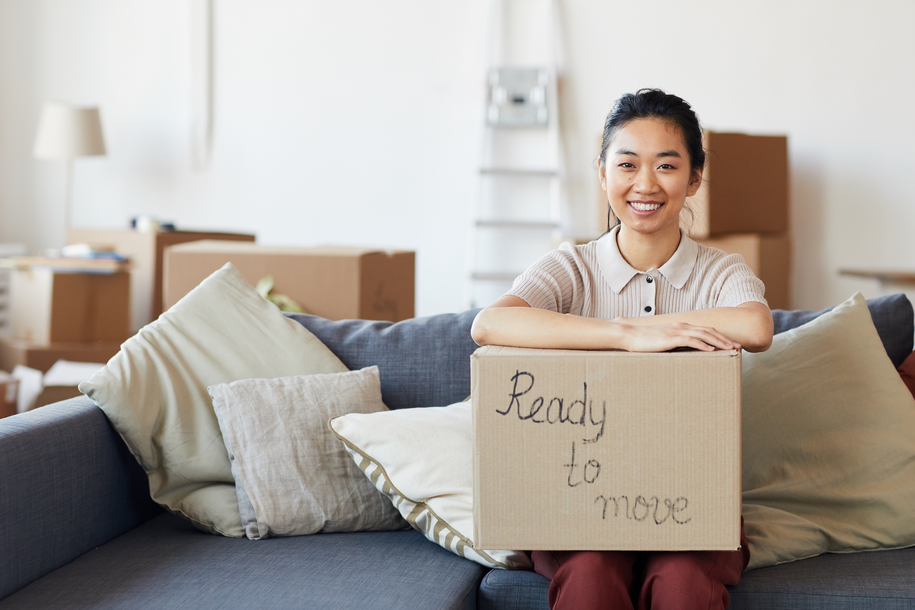 A smiling resident sitting on a sofa with a moving box at Lofts at Wolf Pen Creek in College Station, TX.
