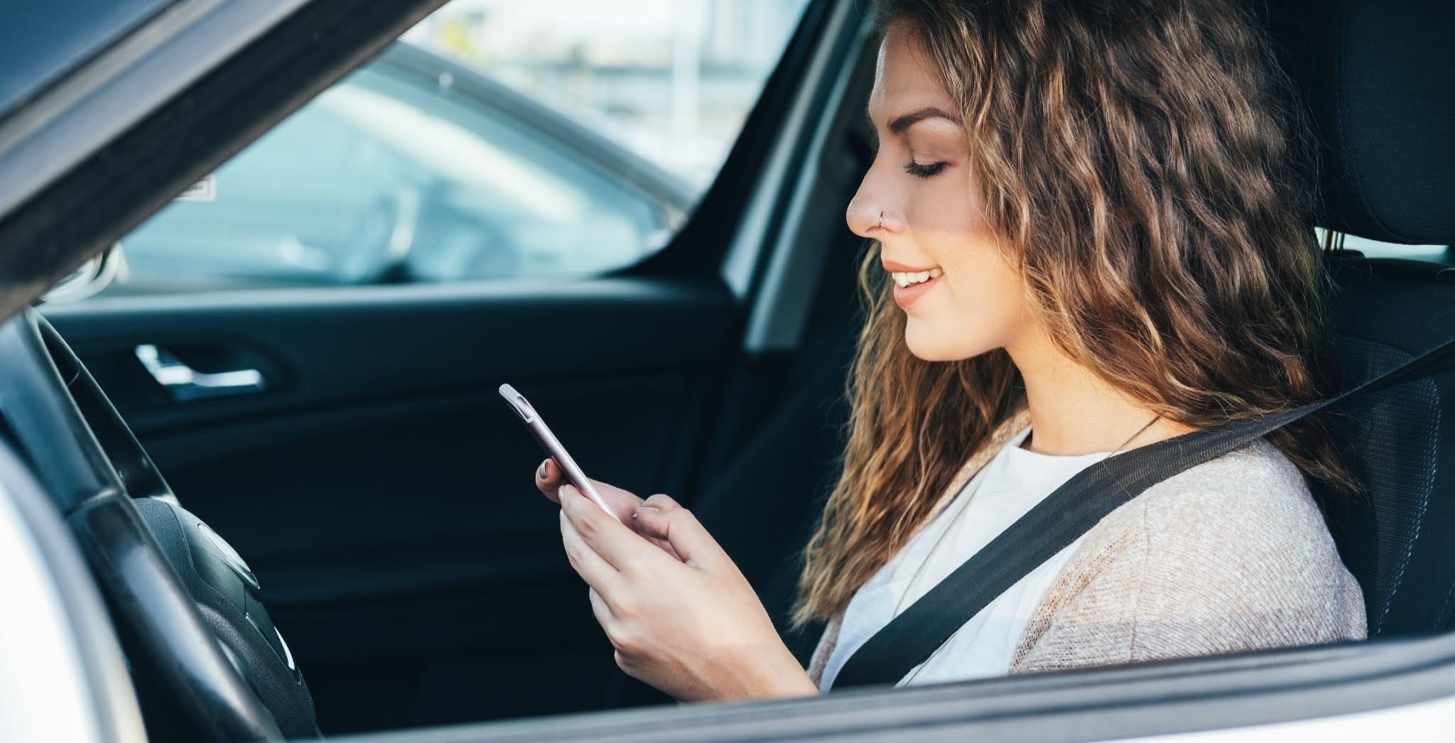 Smiling person in a car looking at a phone with the seatbelt on