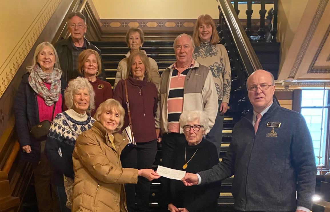 Man with Michigan State Capitol sweater with group of ten people, positioned together for a group photo on a set of decorative stairs.