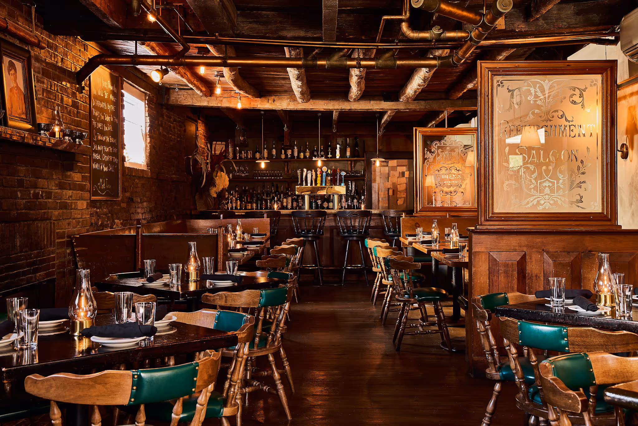 A rustic restaurant interior with wooden tables and chairs, set for dining, and a bar area in the background.