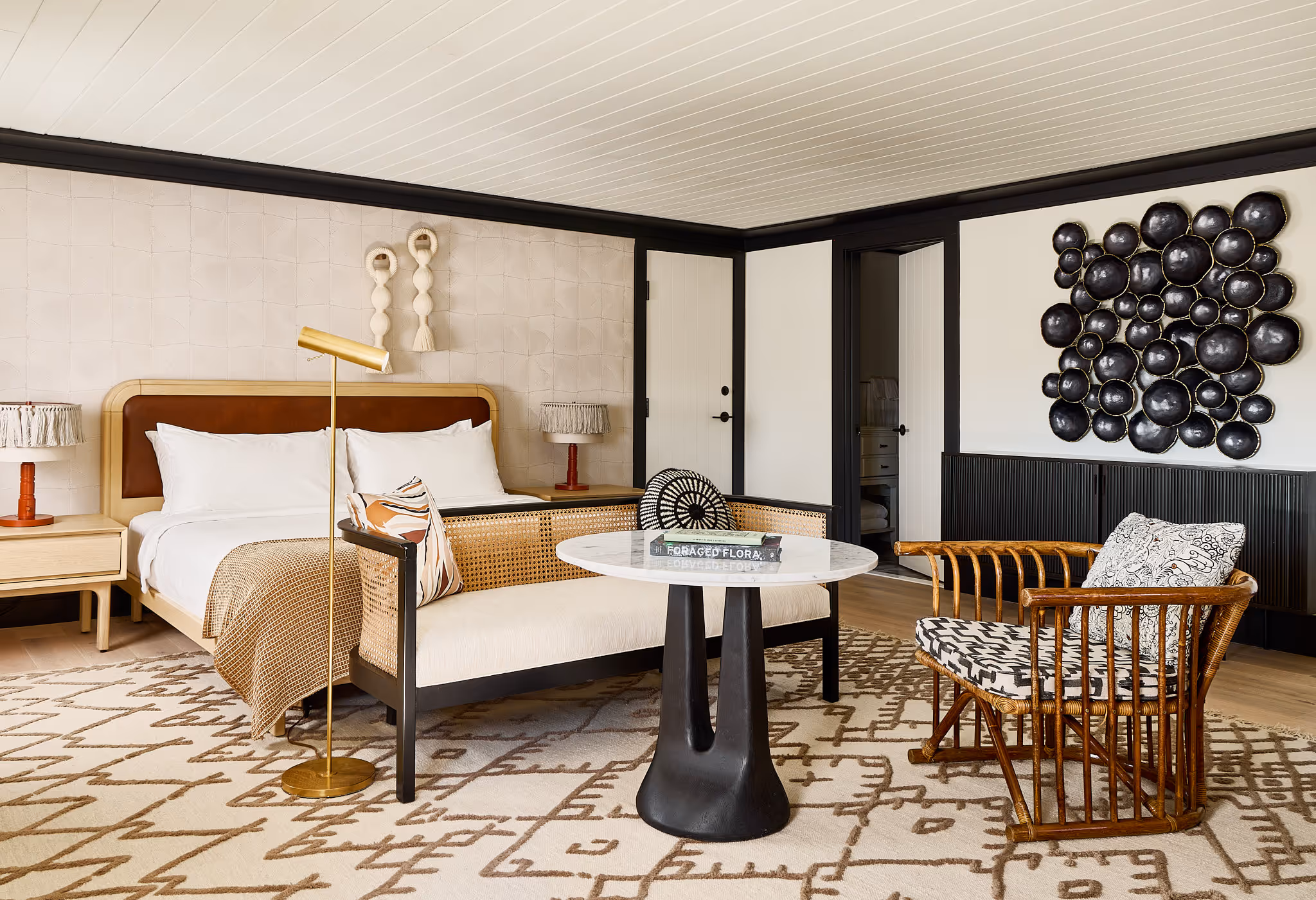 A modern bedroom with a large bed, patterned rug, lounge chair, round table, and contemporary wall decor.