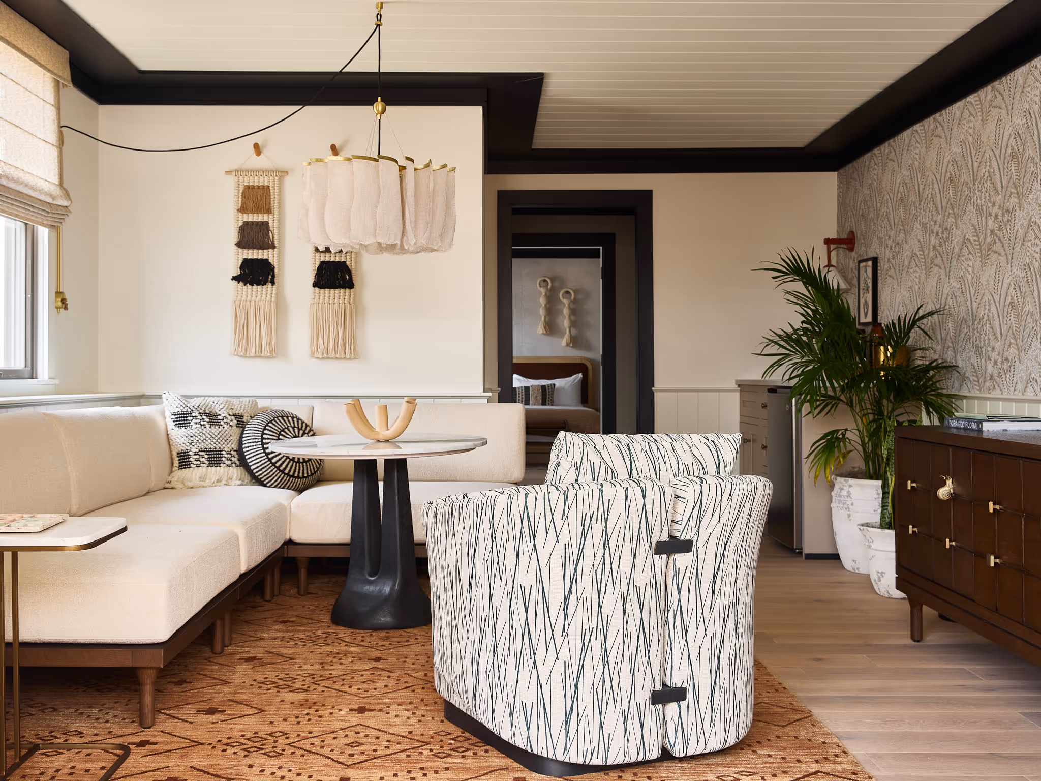 Modern living room with a beige sectional, two patterned chairs, round table, wall art, indoor plant, and patterned rug.
