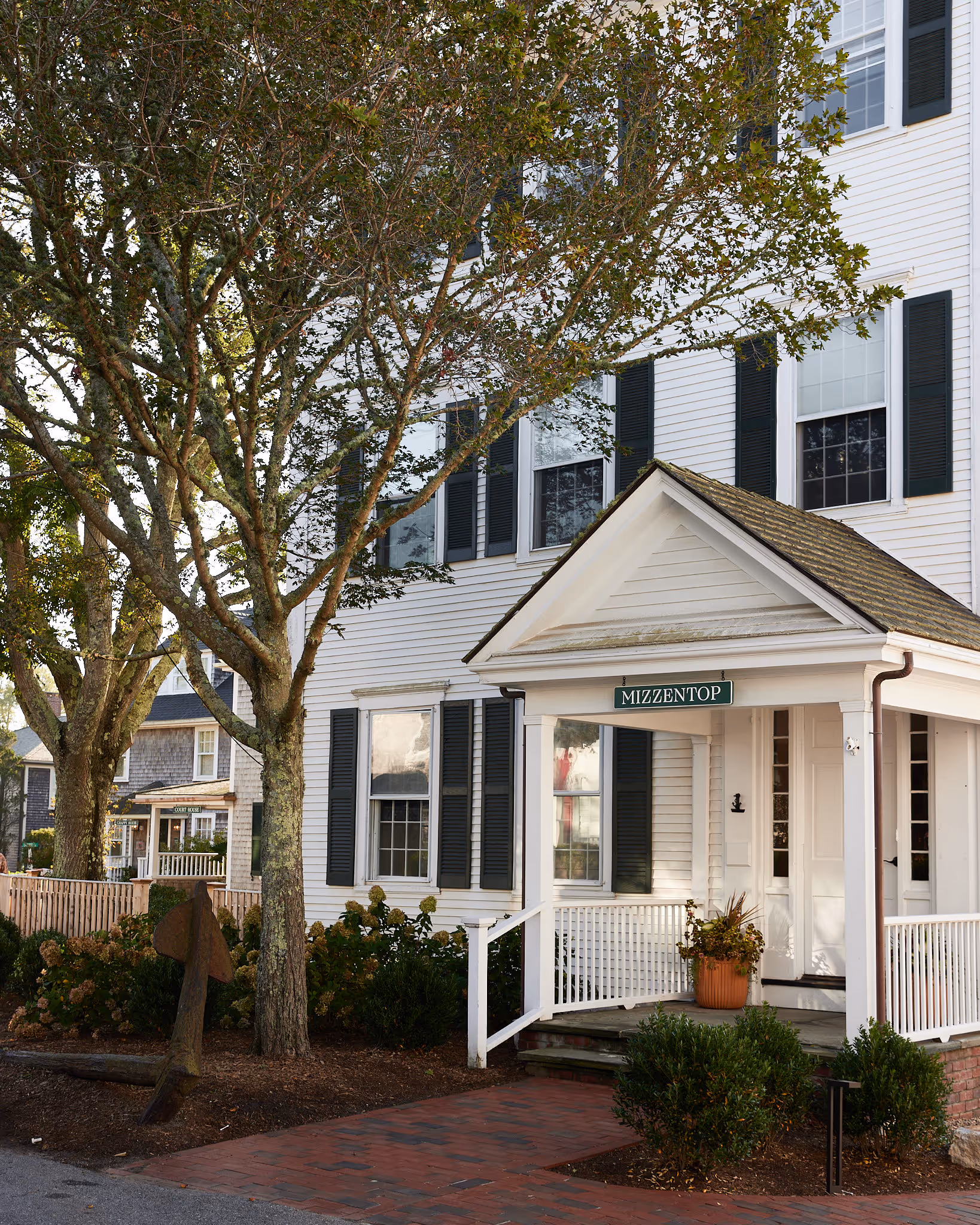 White house with dark shutters, front porch labeled MIZZENTOP, and a large tree in the foreground.