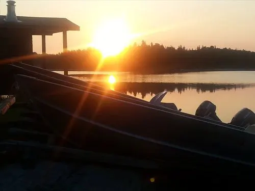 Sunset over Confusion Lake, with aluminum fishing boats moored at the dock and the outpost cabin silhouetted at left.