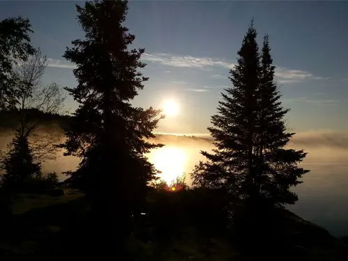Sunrise over Confusion Lake, with mist hovering above the water and tall conifers silhouetted against the glowing sky.