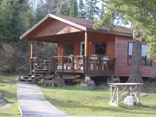 Wilderness Air Escapes outpost cabin at Confusion Lake, showing a wood-sided cabin with covered veranda, deck chairs, and boardwalk path.