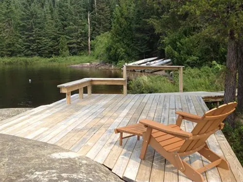 Wooden dock with an Adirondack chair and bench overlooking a calm forested lake at Crooked Lake outpost.