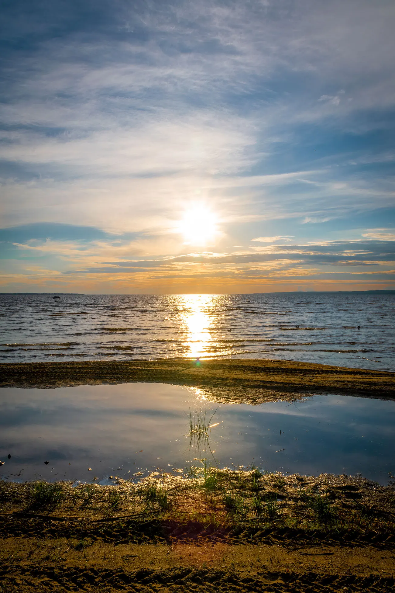 Golden sunset over Pilot Lake, with sun glare reflected across calm water and a tidal pool on the sandy shore.