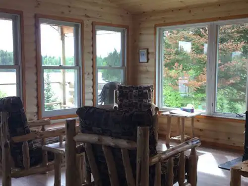 Interior of the Sup Lake outpost cabin with rustic log furniture and large windows overlooking a forested shoreline.