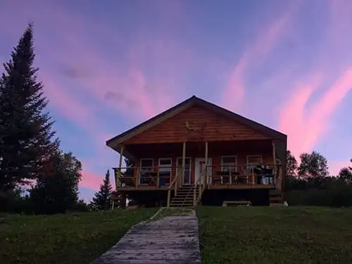 Sup Lake outpost cabin at dusk, bathed in pink and purple sky, with a wooden walkway leading to the front deck.
