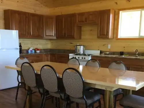 Interior of the Sup Lake outpost cabin kitchen, with wood cabinets, gas stove, white fridge, and a large dining table with six chairs.