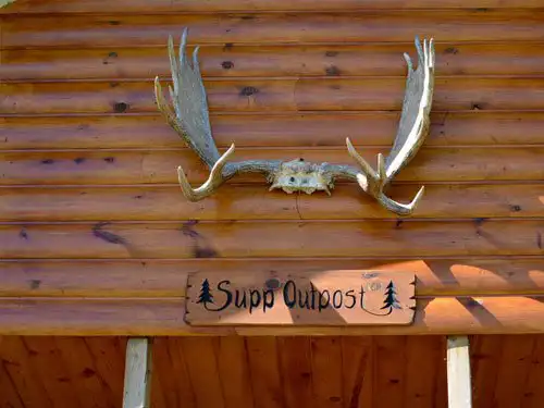 Moose antler mount above a wooden sign reading Supp Outpost on the cedar-sided wall of the Sup Lake outpost cabin.
