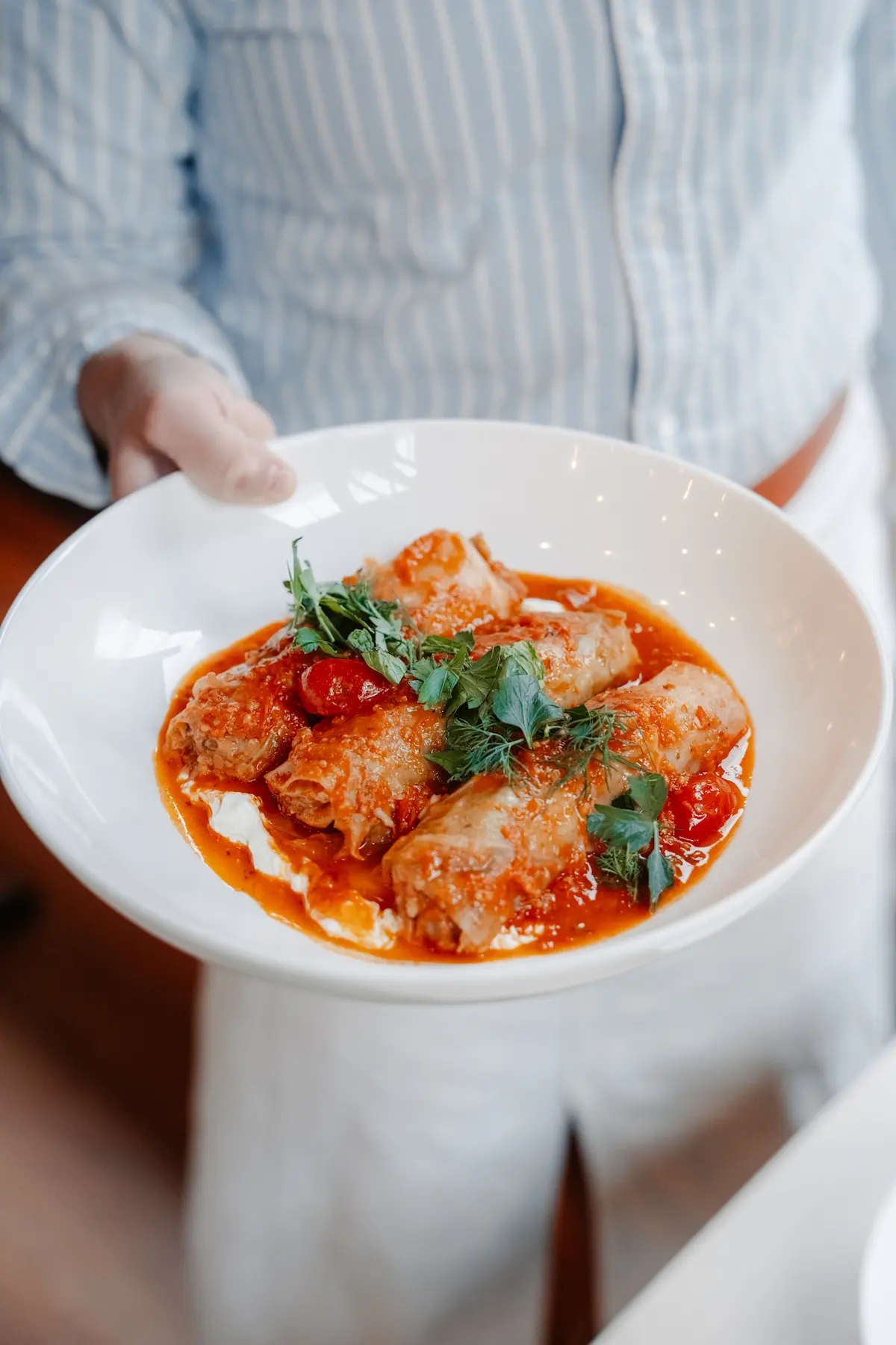 Cabbage rolls in rich tomato sauce topped with fresh herbs, served on a white plate.
