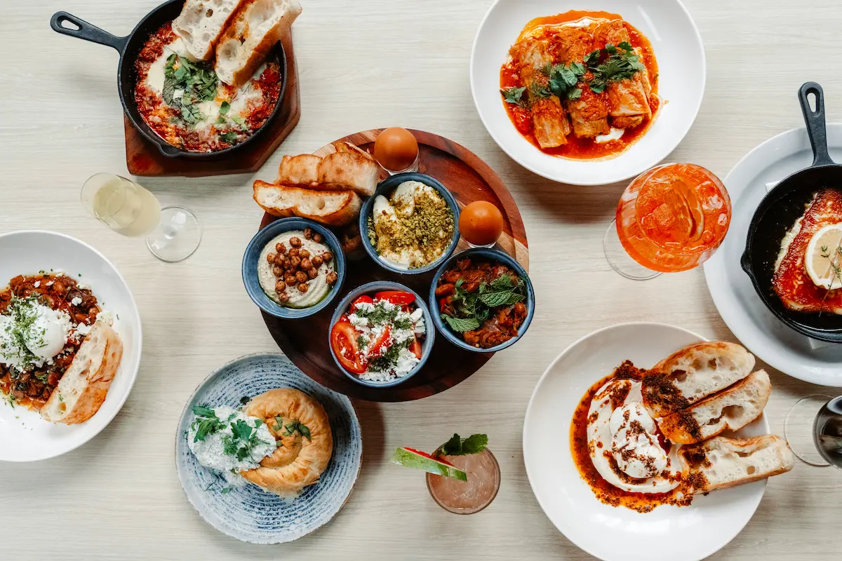 Flatlay of a Mediterranean feast with dips, eggs, breads, and cocktails on a table.