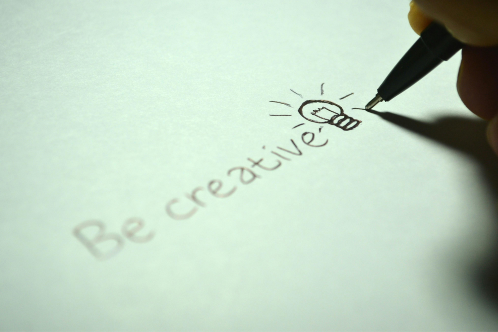 Hand drawing a lightbulb and writing 'Be creative' on paper.