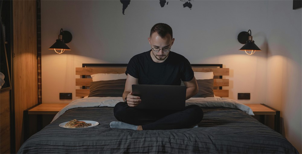 Person working on a laptop while sitting on a bed.