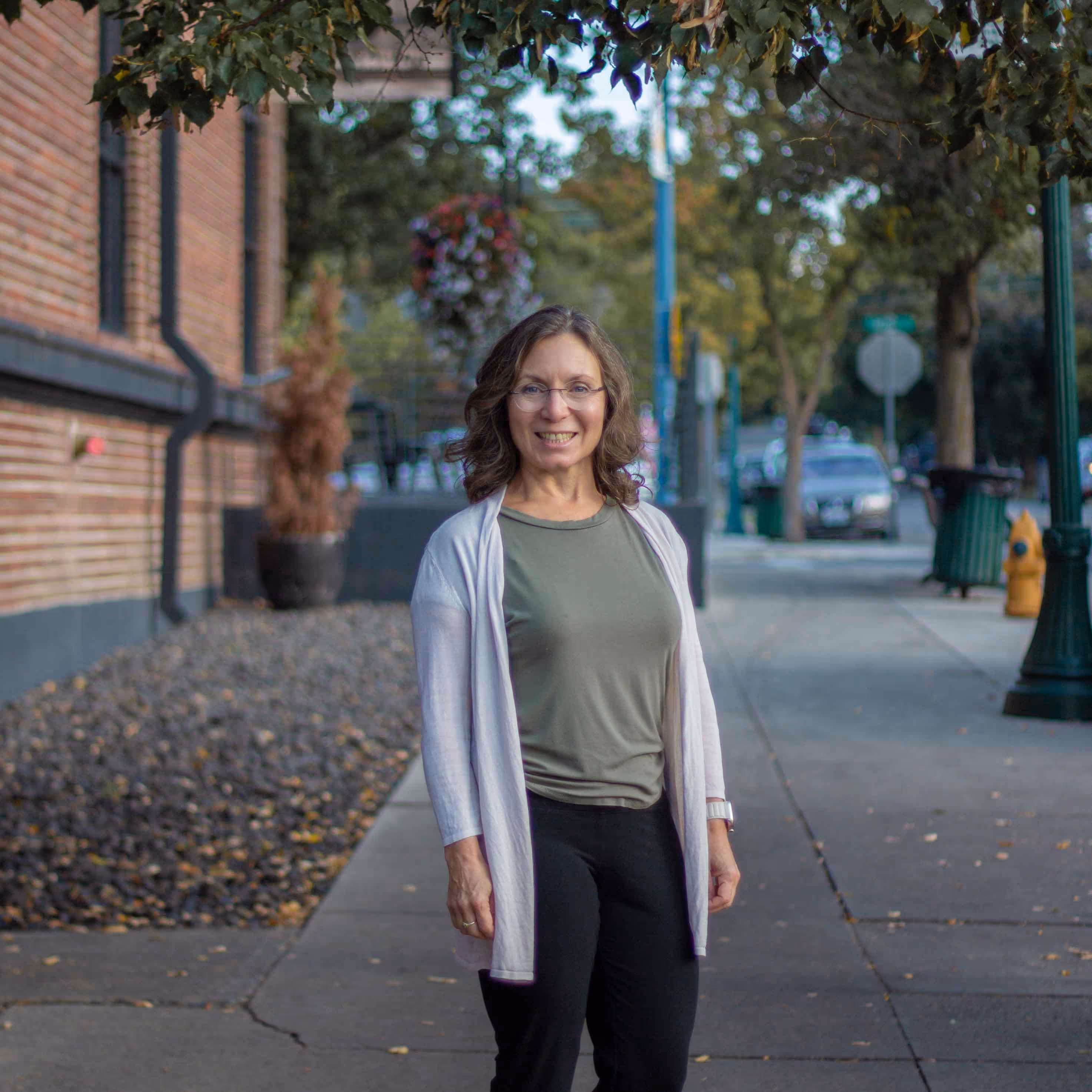 Smiling woman on a sidewalk with trees in the background by Inlumina Creative.